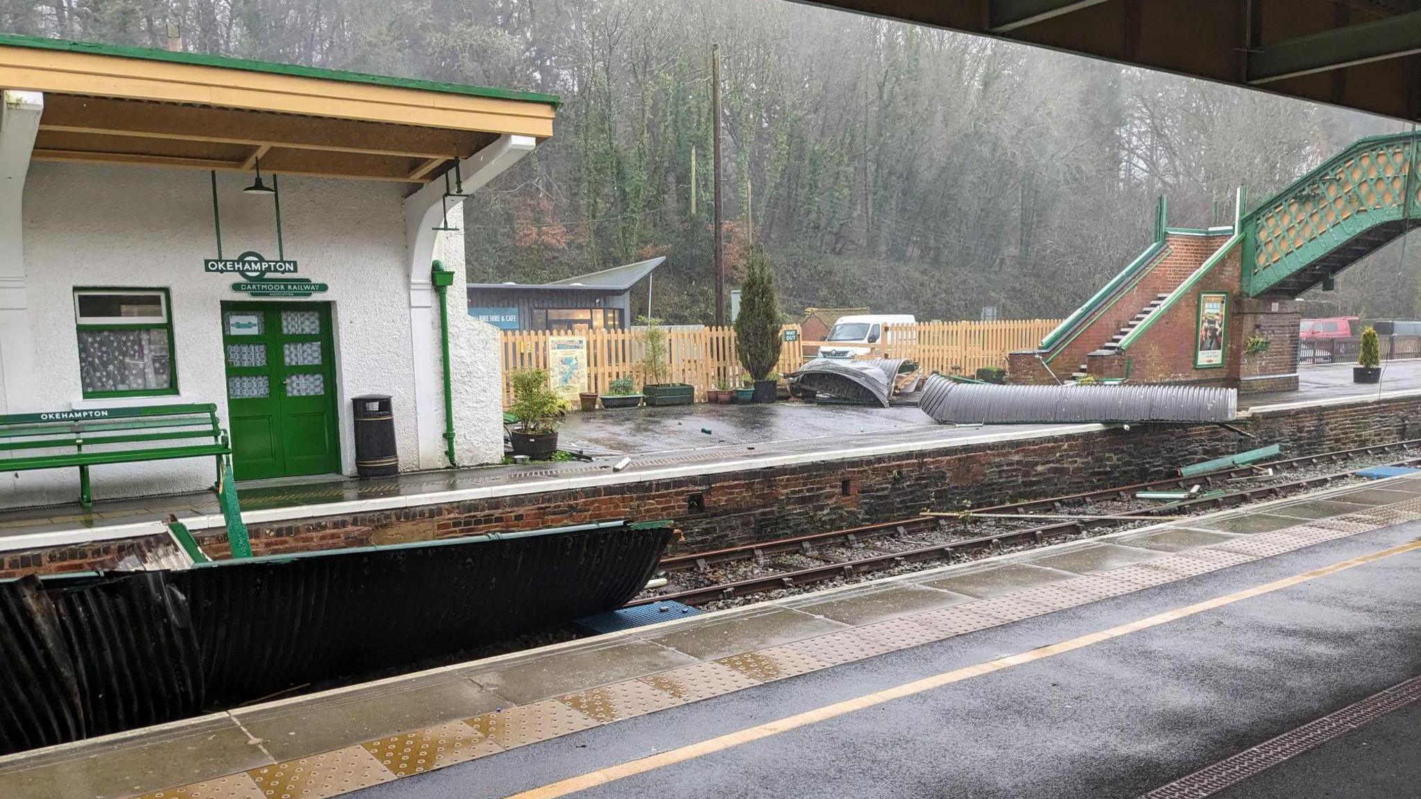 A wet Okehampton train station has large pieces of debris strewn across its platforms and the railway tracks during Storm Henk.