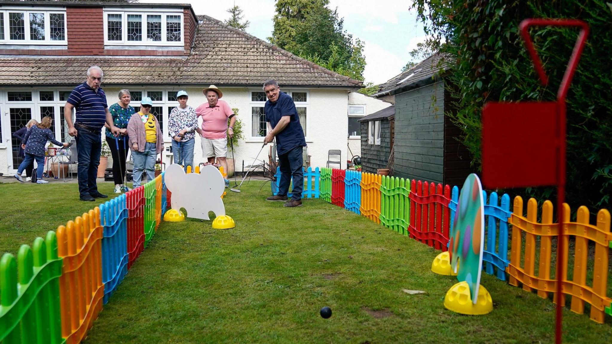 The course in use by a group of people with a brightly coloured fence seen along the edges and a golf ball bouncing towards the camera