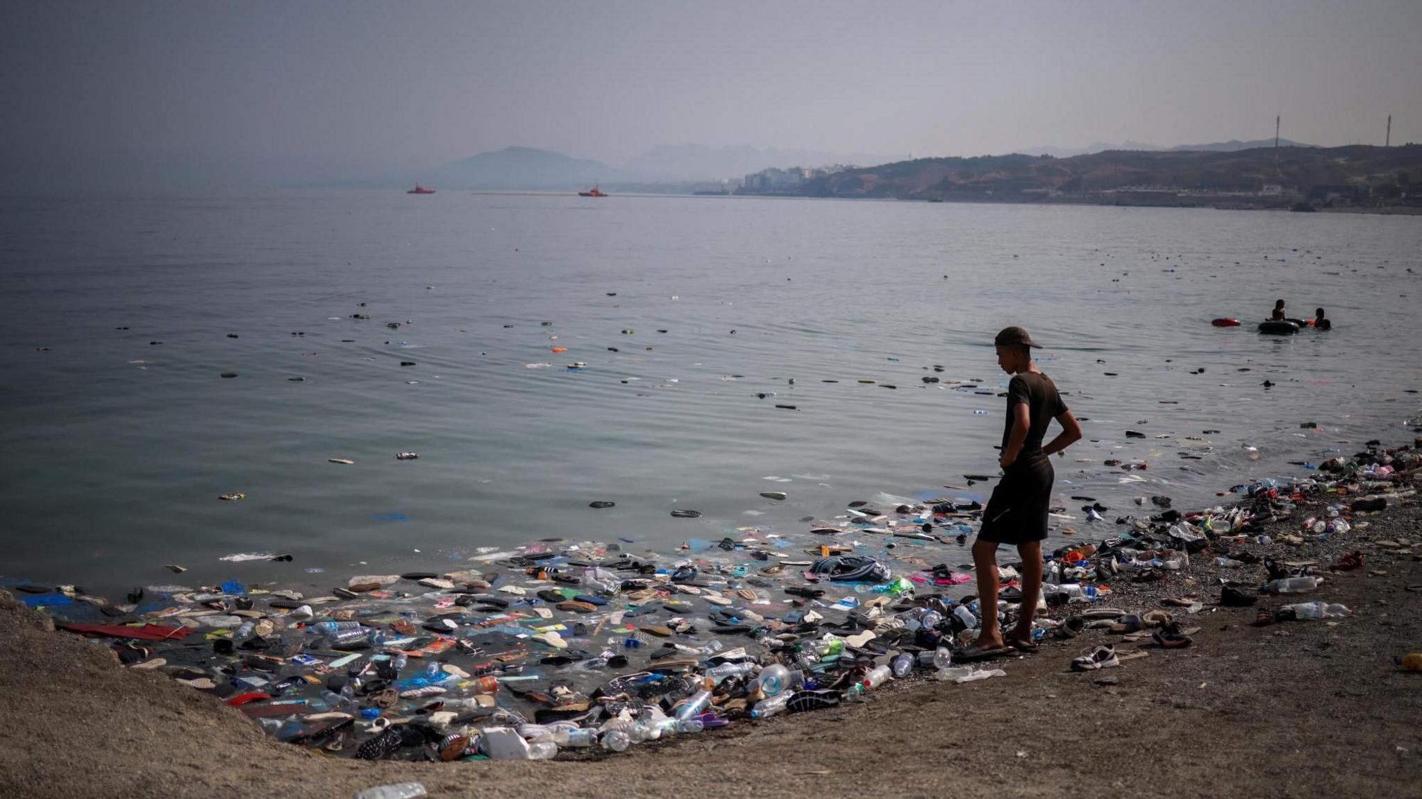 A migrant looks at the sneakers on the water following mass crossings of migrants on foot and by sea from Morocco into Spanish territory.
