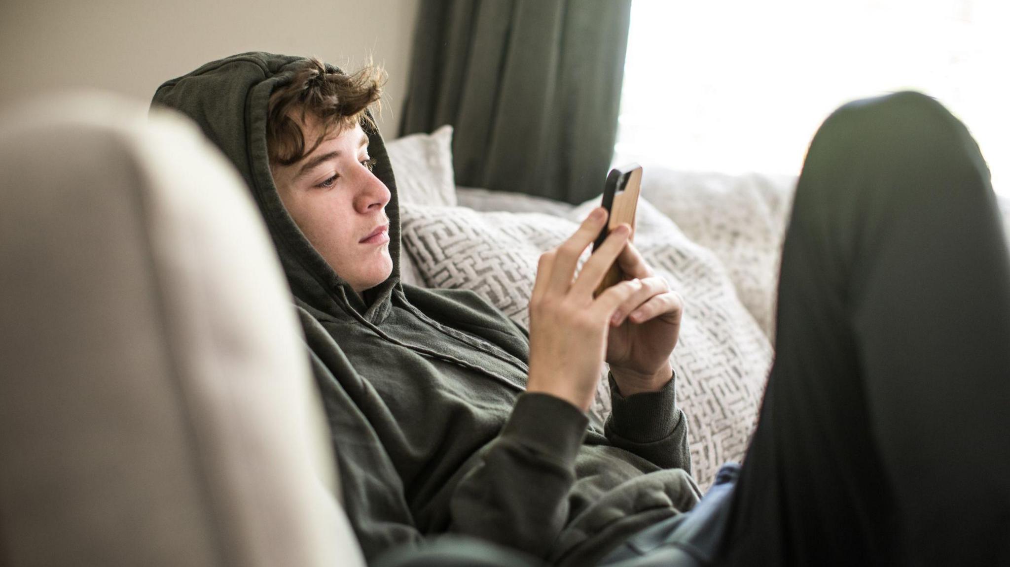 Boy on sofa looking at smartphone. 