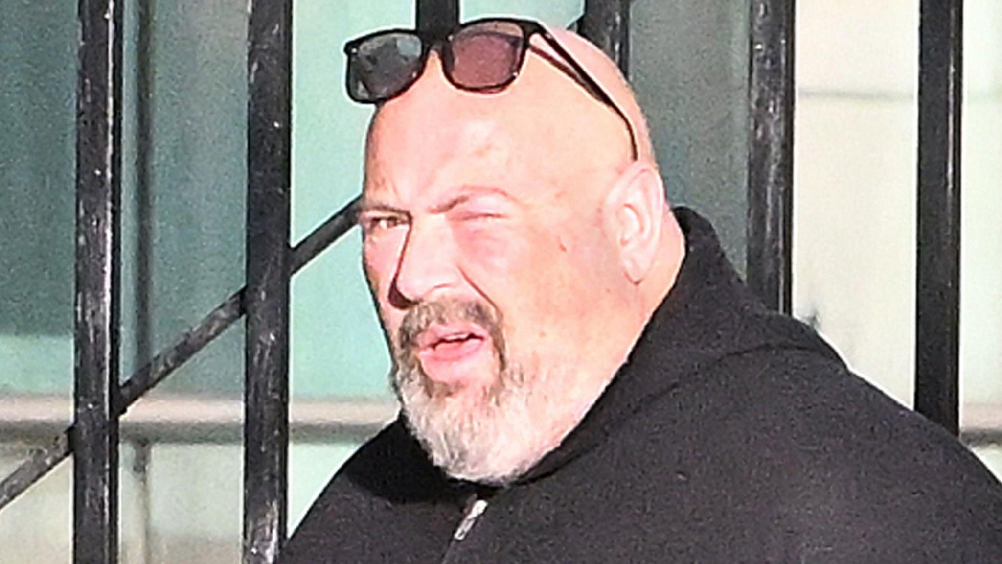 Shows a man with beard and dark hooded-top with glasses above his head 