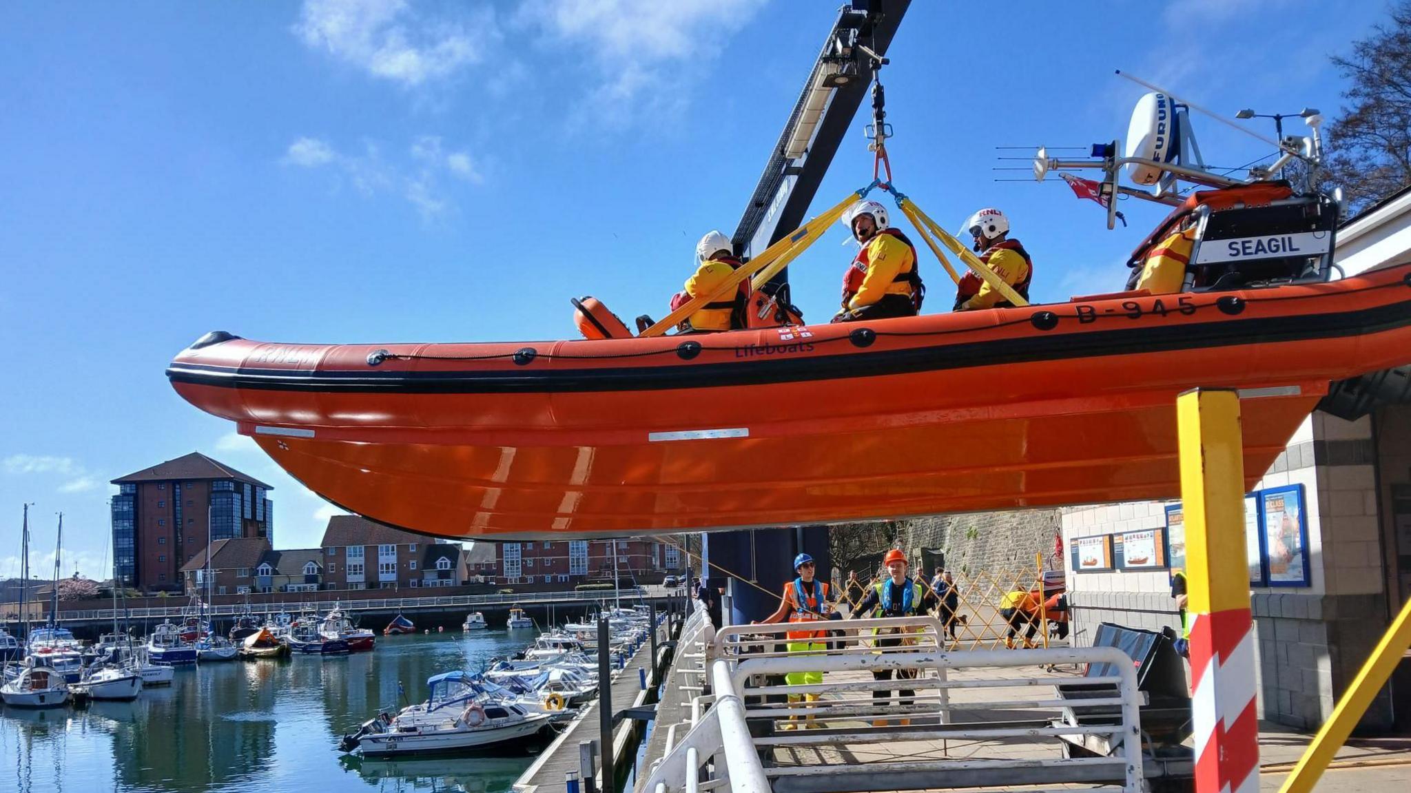 An orange RNLI lifeboat with three crew on board being lowered into the water at Sunderland Marina. 