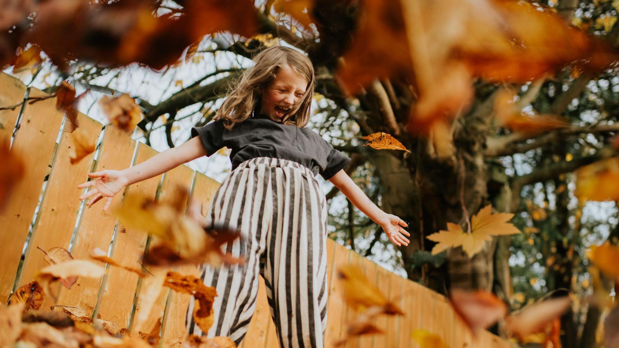 Girl playing in orange leaves