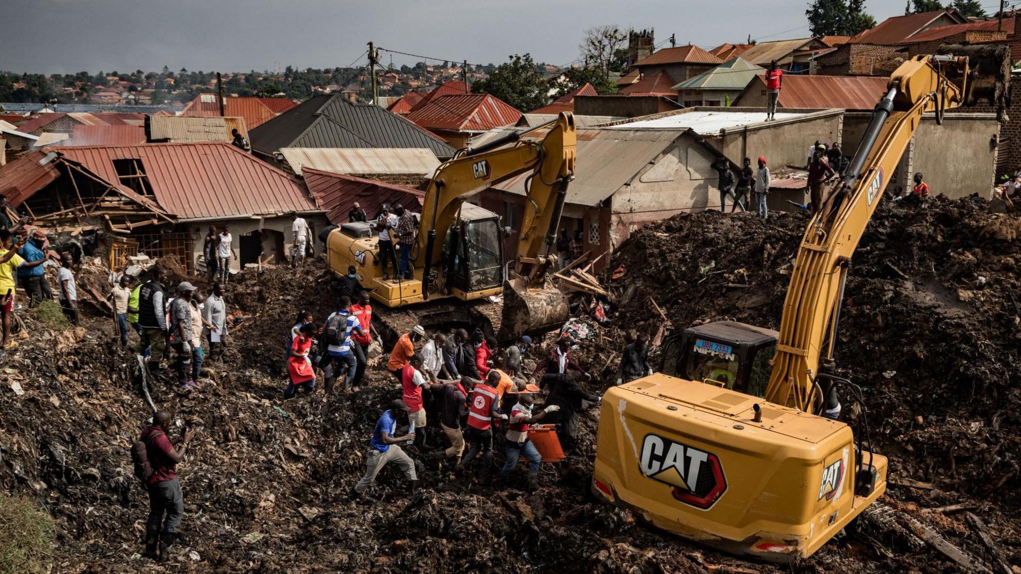 Two diggers and rescue workers dig through huge piles of rubbish