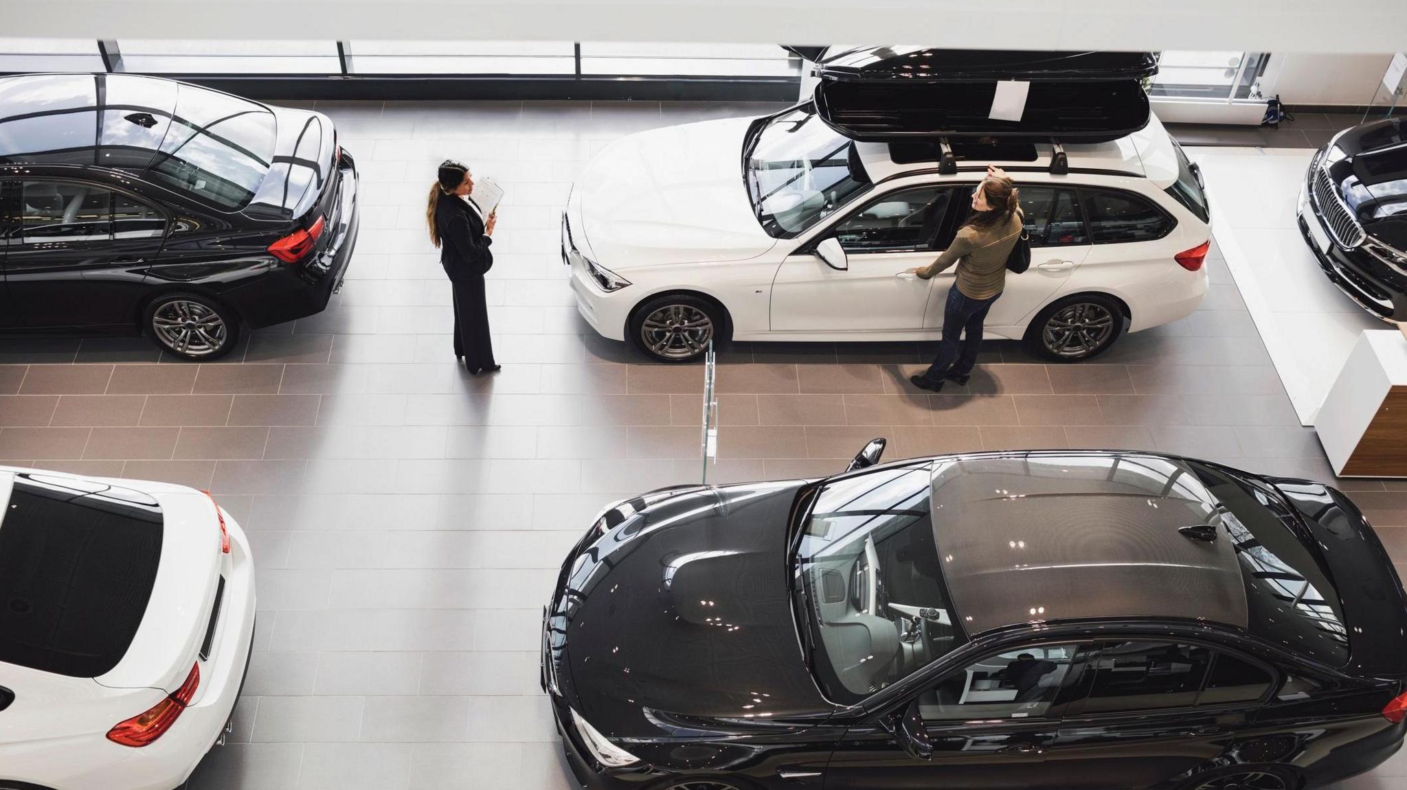 Overhead view of a woman looking at a car in a showroom with a dealer standing nearby