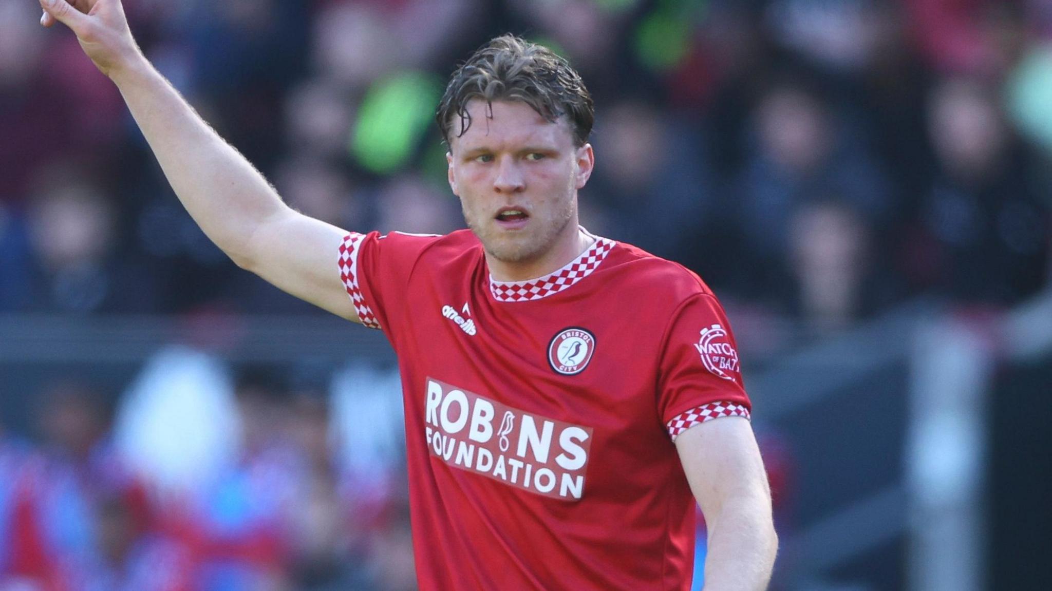 Bristol City defender Rob Dickie, with his right arm aloft. He has short dark hair and is wearing the red home kit of Bristol City.