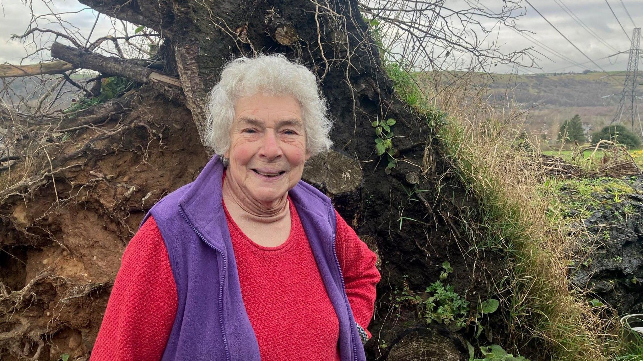 Photograph of woman in front of a tree which was uprooted by the Stalybridge tornado