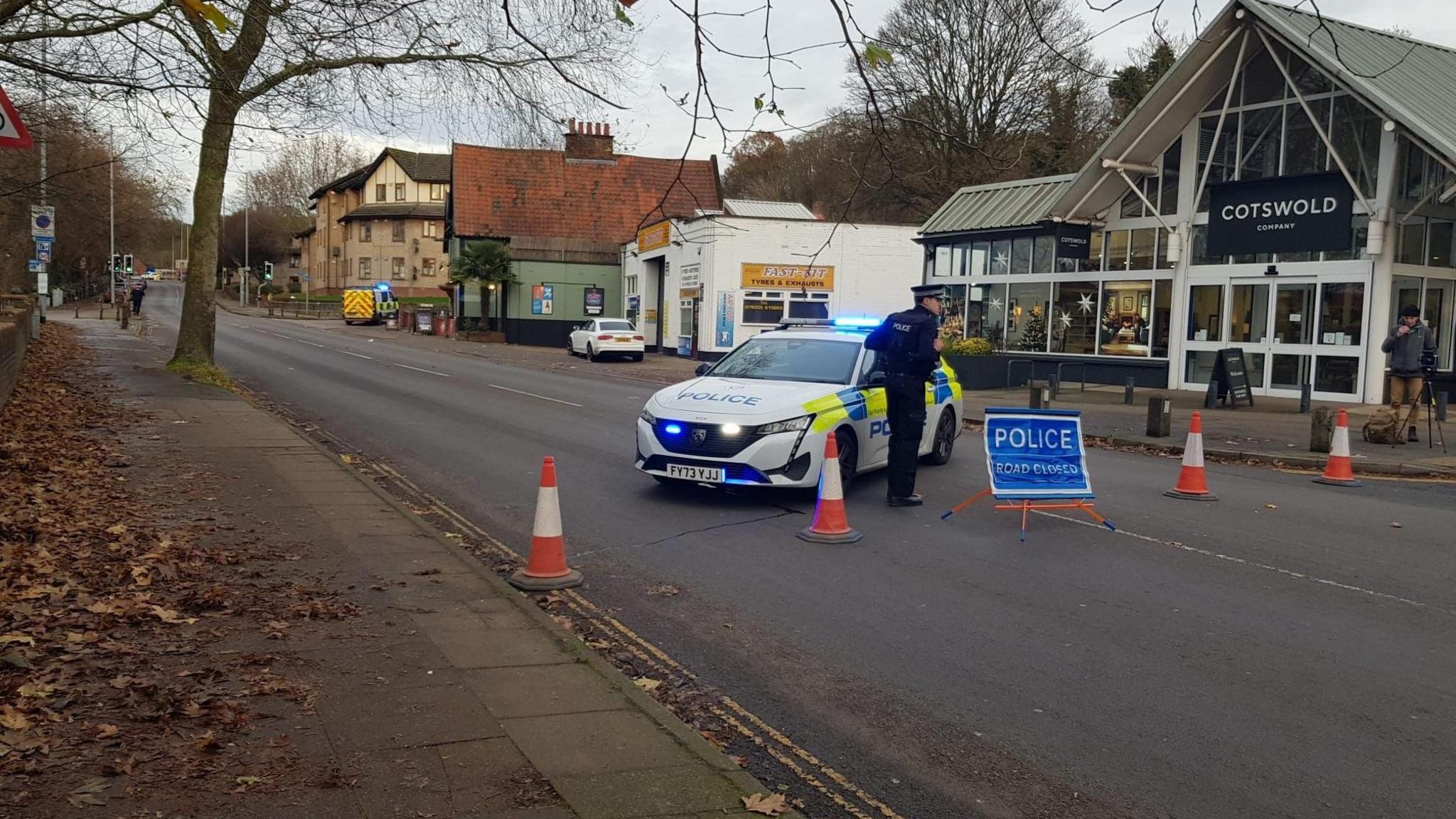 A street view image of a police car parked in the middle with a blue police sign 