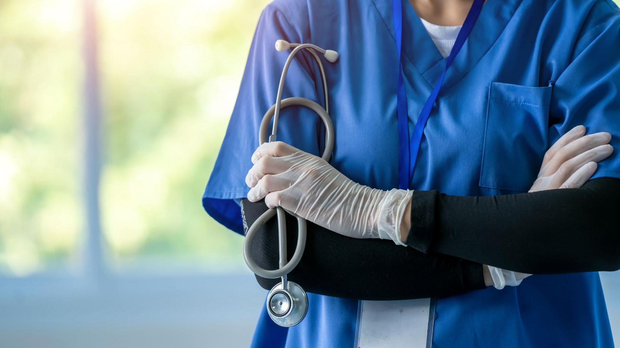 A female doctor, pictured from the neck down, in blue scrubs with stethoscope around her neck