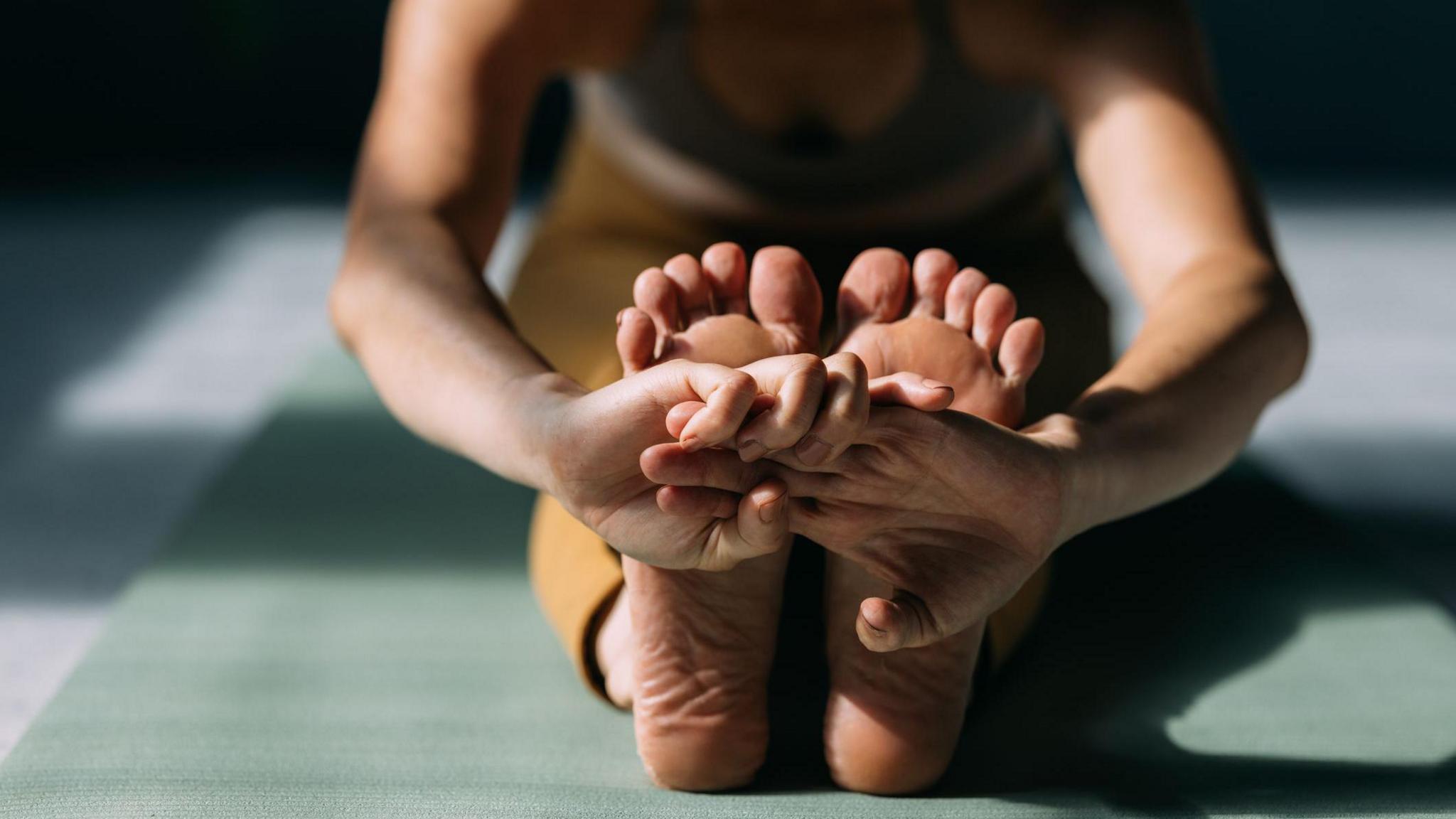 A stock picture of a woman - just her feet and body fully in picture - stretching her legs while doing yoga