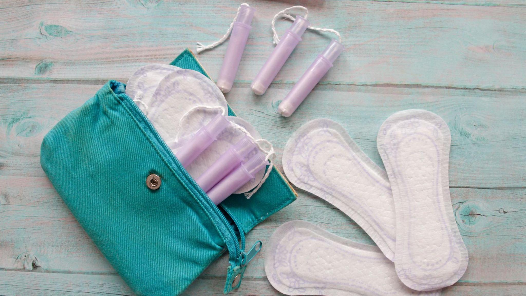 Sanitary pads and tampons, lying on a surface, with some item in a green purse