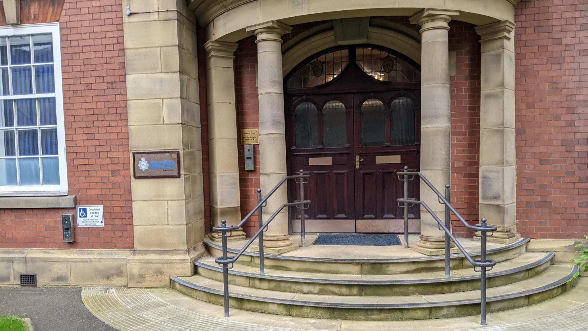 West Yorkshire Police HQ in Wakefield. Pictured is a set of oak-coloured double doors between two Roman style pillars. The police logo features to the left of the doors