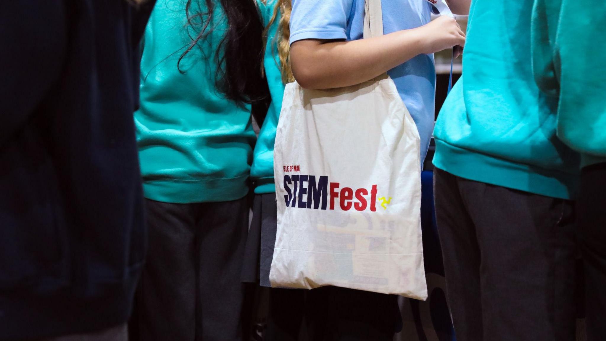 A closeup of a girl with a white cloth bag over her shoulder that has STEMFest written on it.