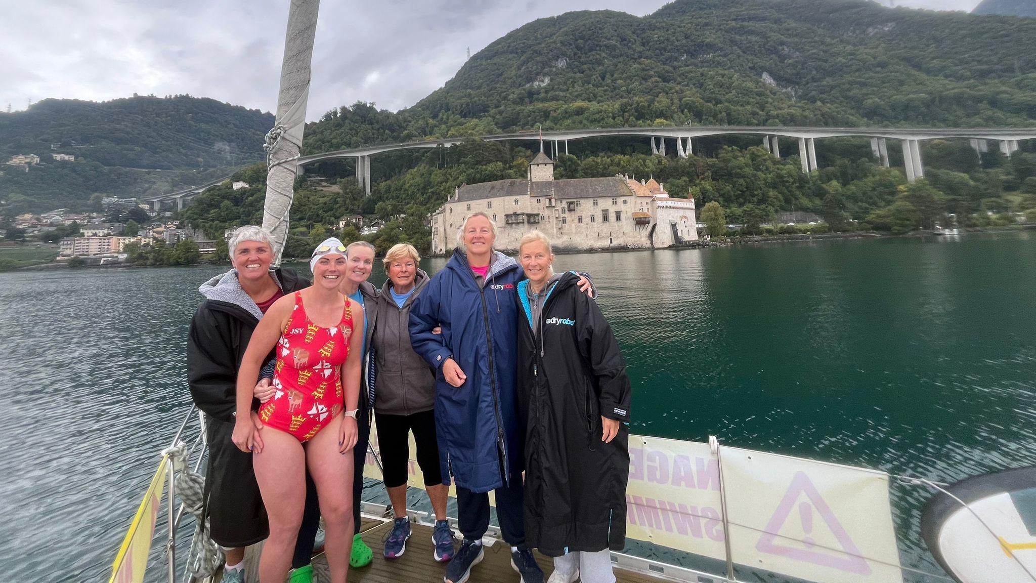 All six swimmers smile at the camera on a boat at the start of the challenge. Five of them are wearing long coats and hoodies. But Alice is her swimming costume with a white swim cap. The Jersey Girls team are holding each other as well.