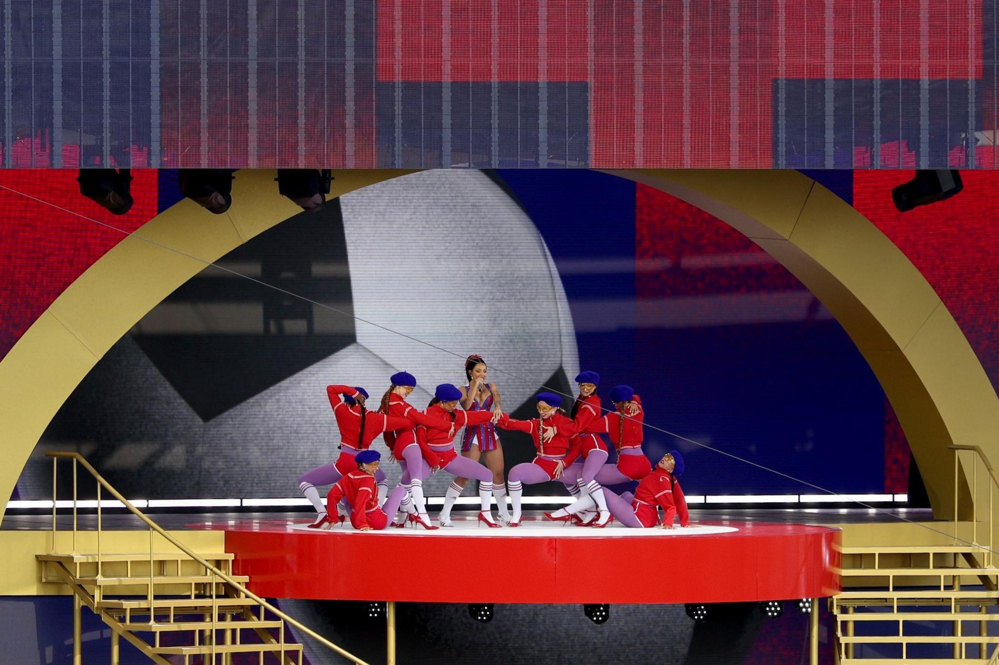 Doja Cat performs during the halftime show at the FIFA Club World Cup 2025 Final match between Chelsea FC and Paris Saint-Germain at MetLife Stadium wearing a short purple and red dress. She is surrounded by dancers in red outfits and purple tights.