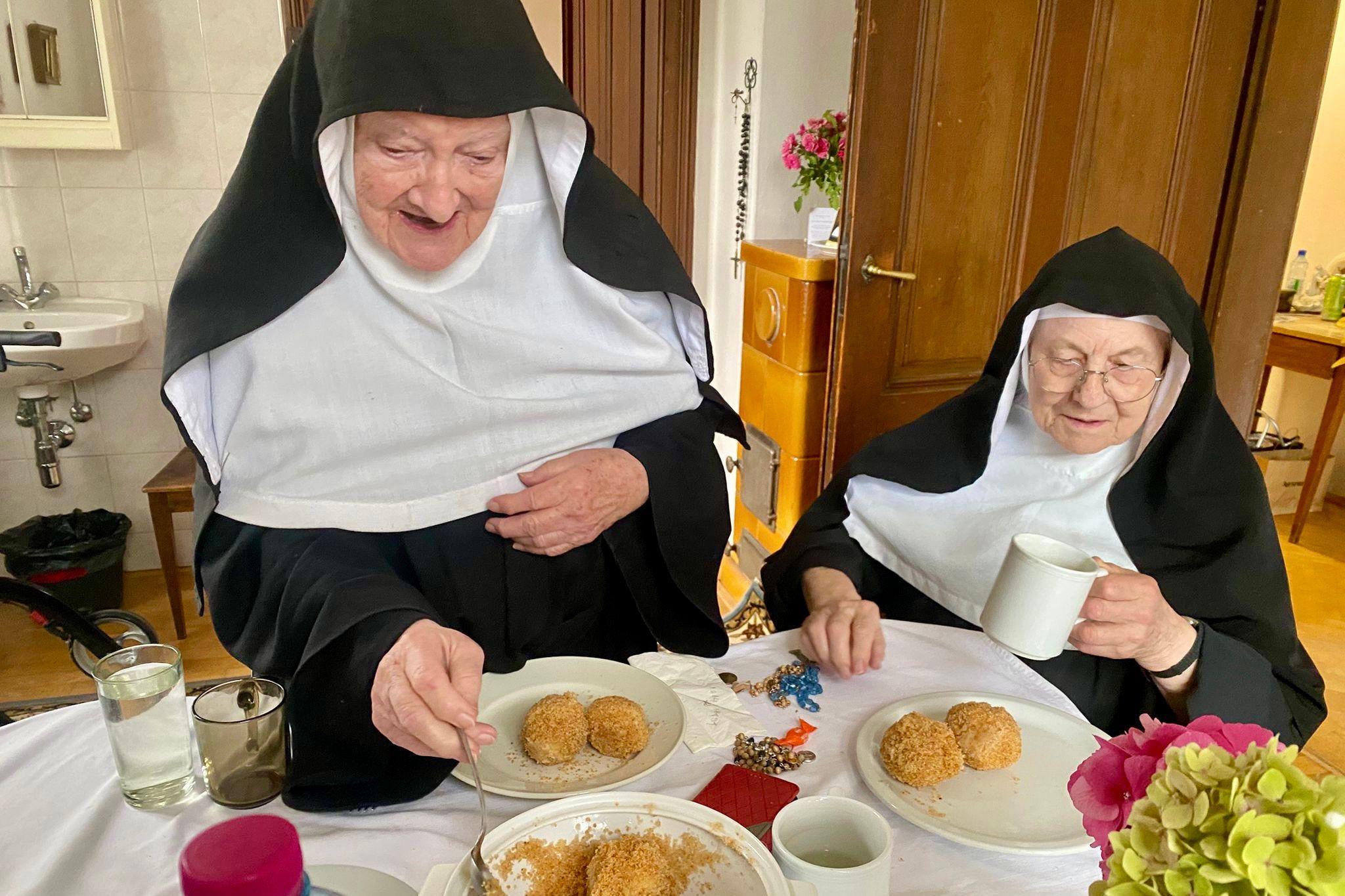 Two nuns have food at dinner as one of them serves it