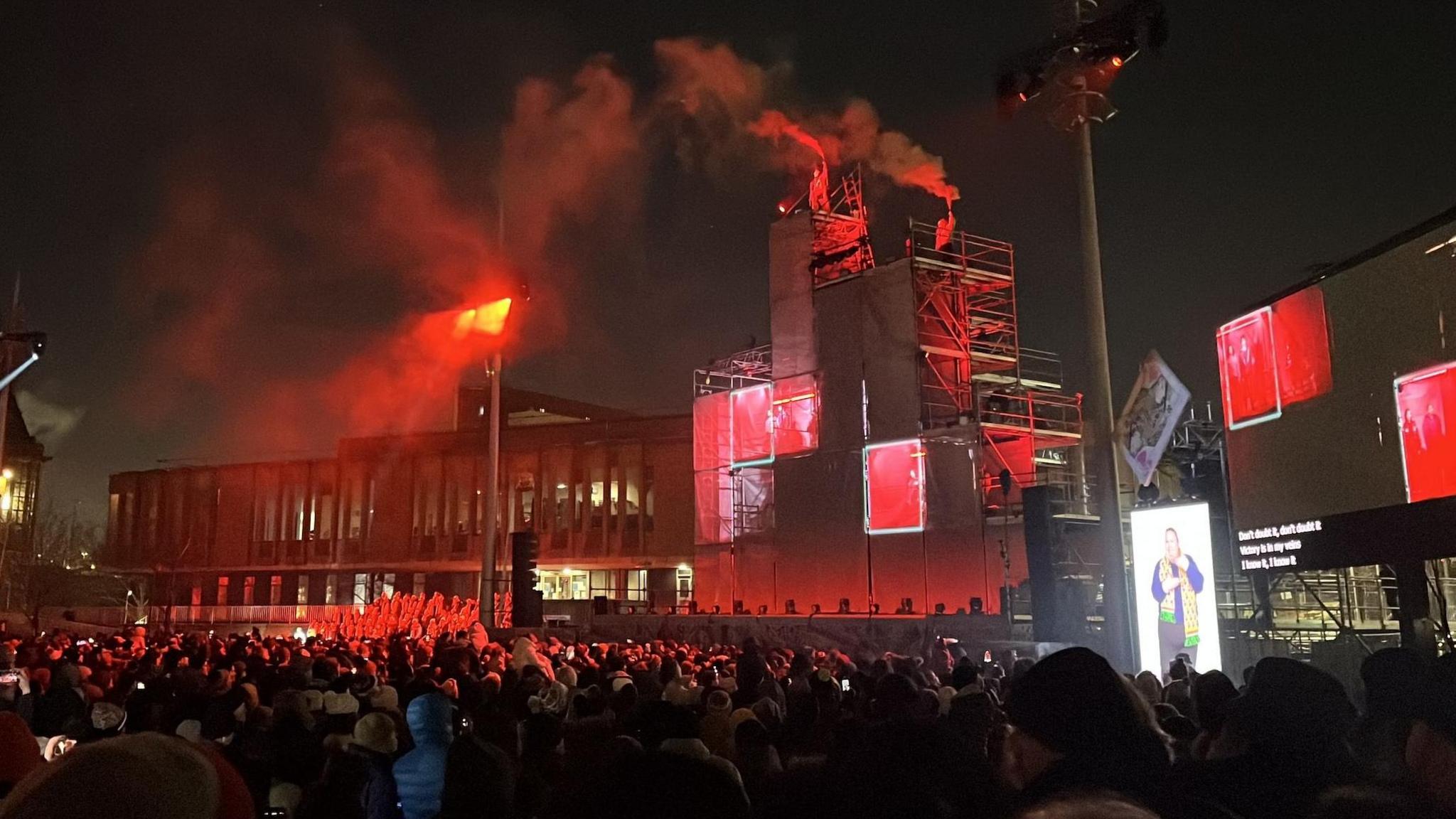 Stage with glowing red boxes as a show kicks off in large public square