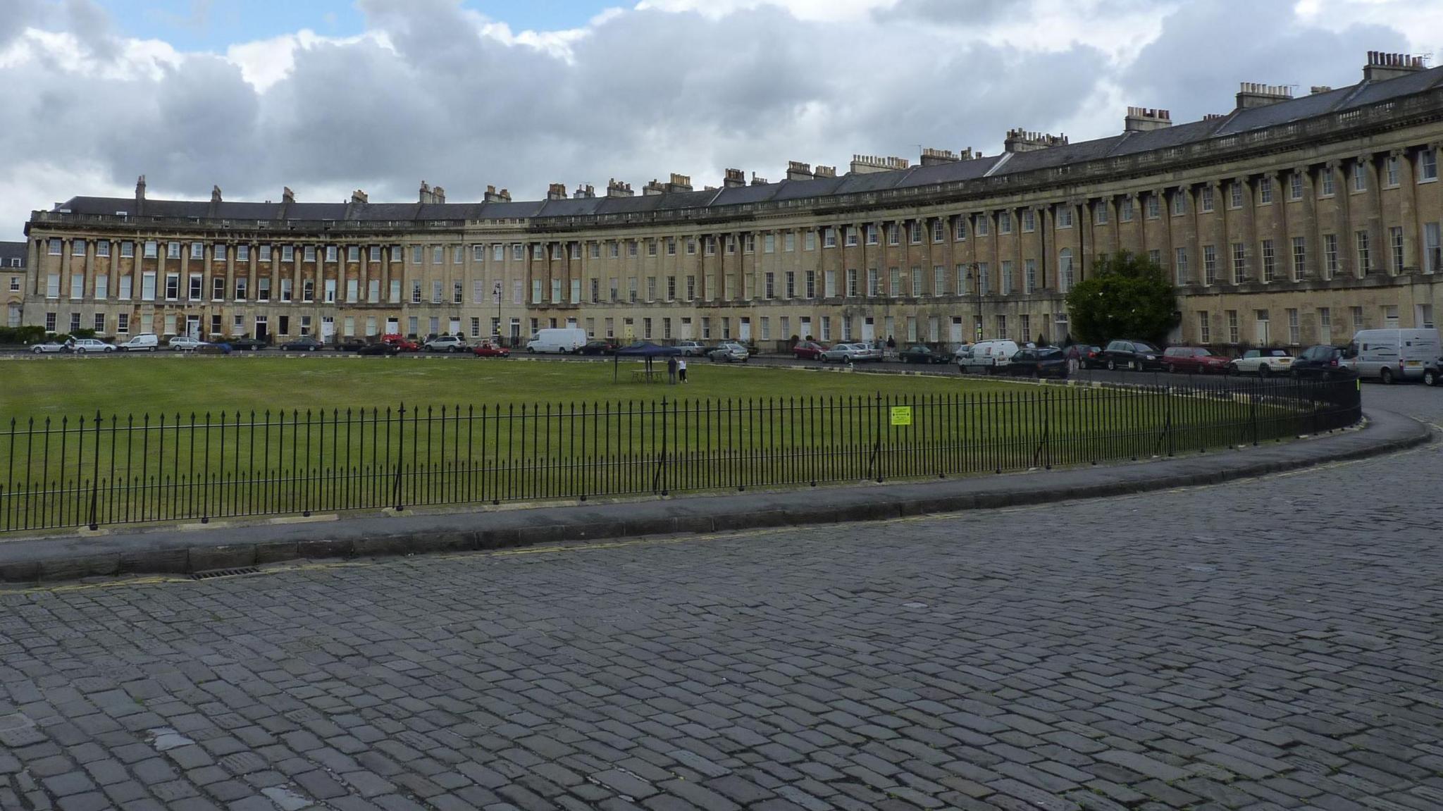 The Royal Crescent in Bath as seen from the street. It is a grand sweeping row of terraced houses with a park and railings in front