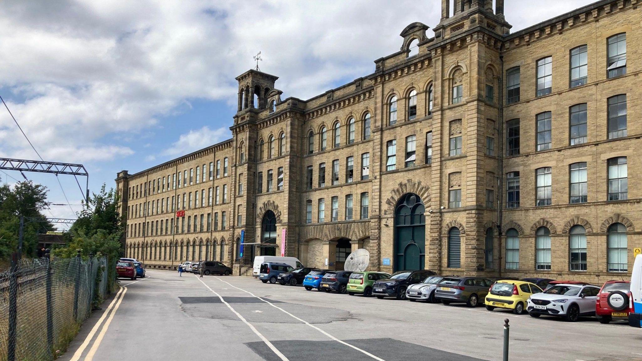 Cars parked outside a large, Victorian mill made from Yorkshire stone.