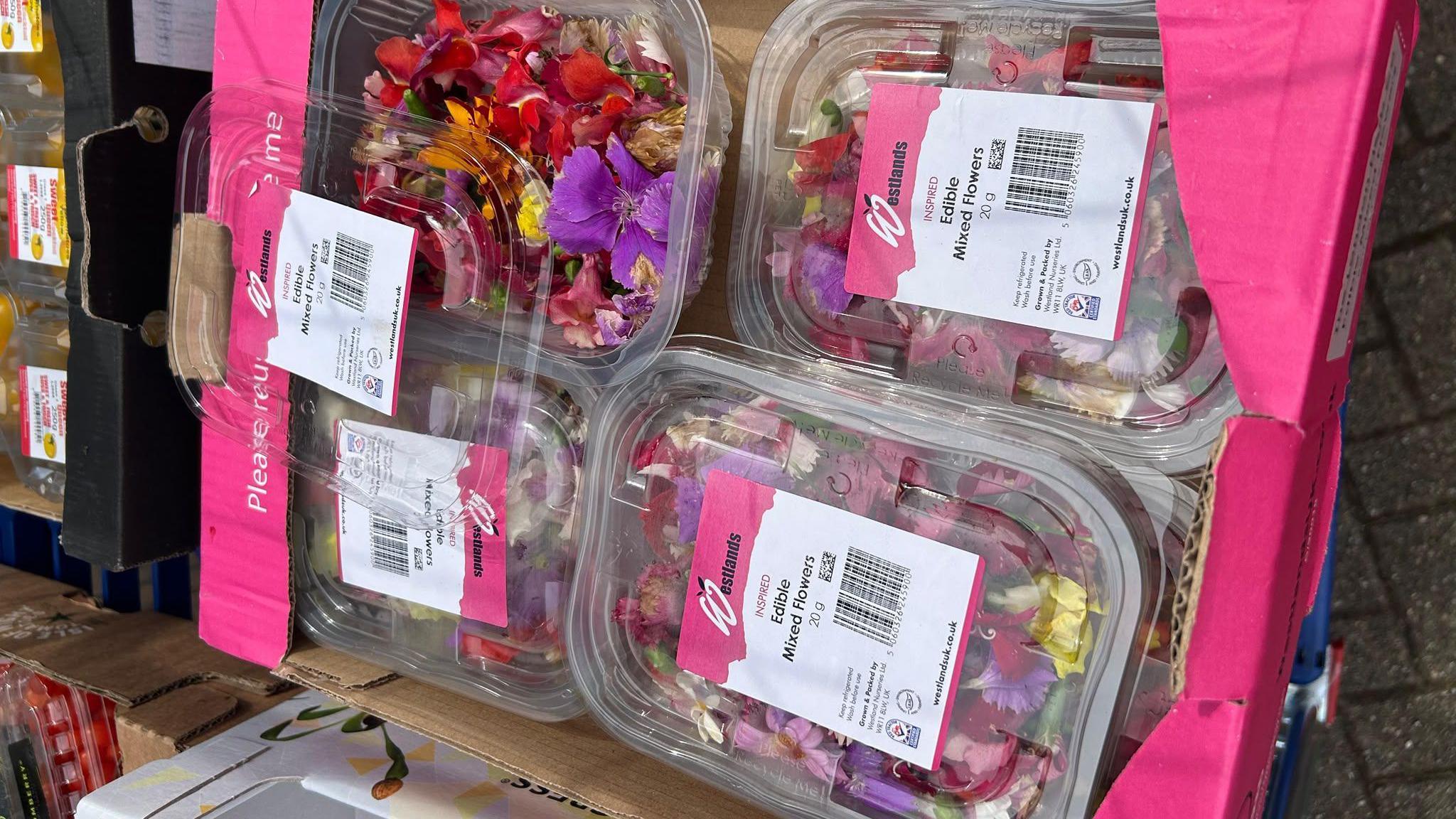 A number of boxed edible mixed flowers, piled up in a pink cardboard box. 