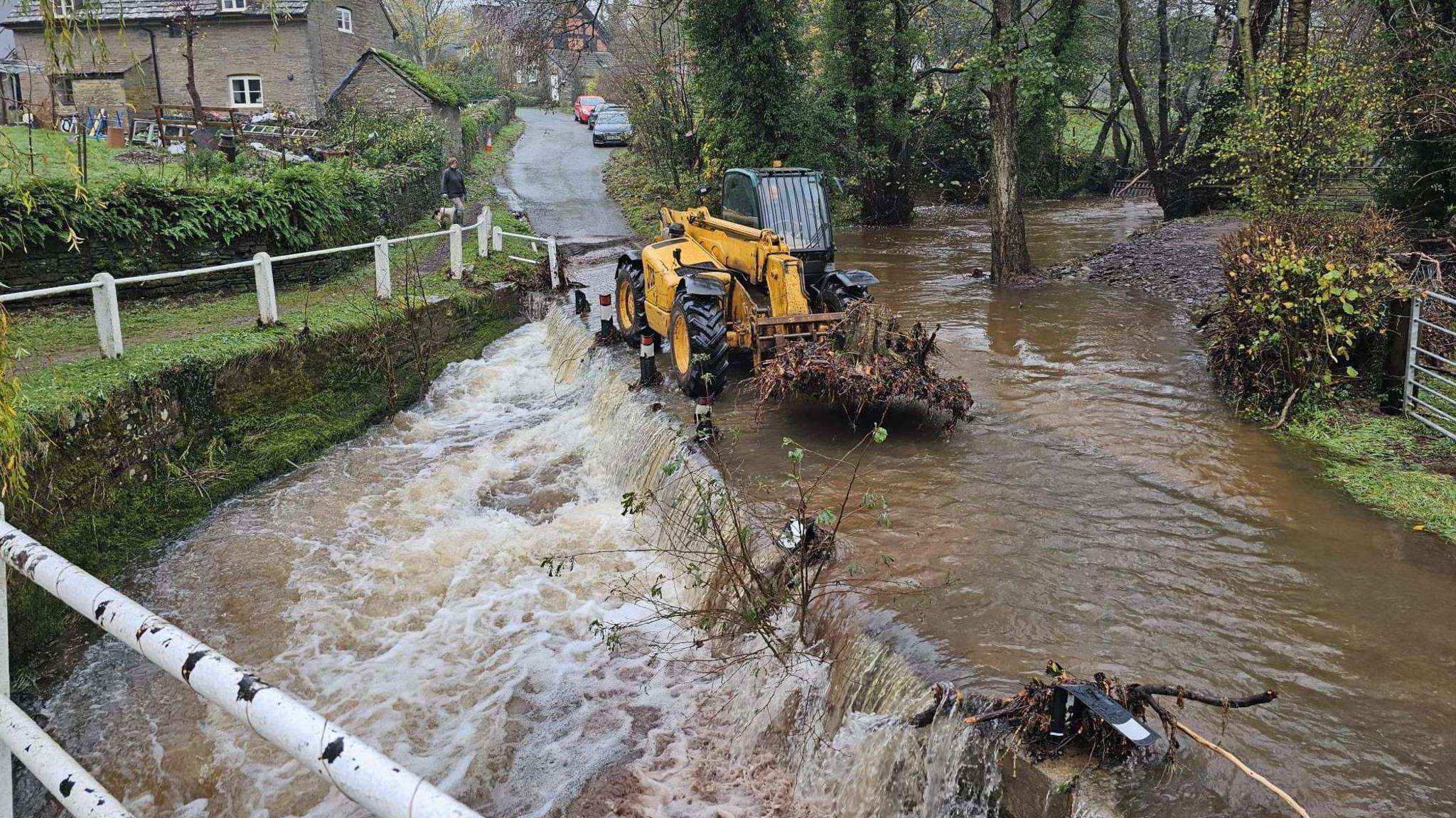 A tractor clearing debris from a flooded road.