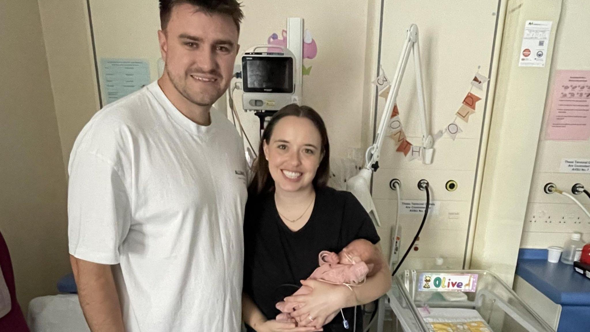 Man standing next to woman holding baby in hospital