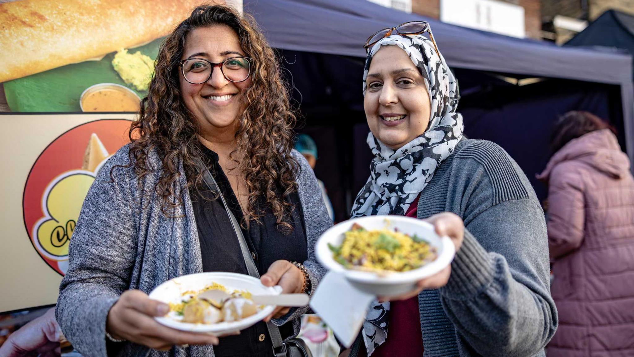 Two women smiling while holding bowls of food