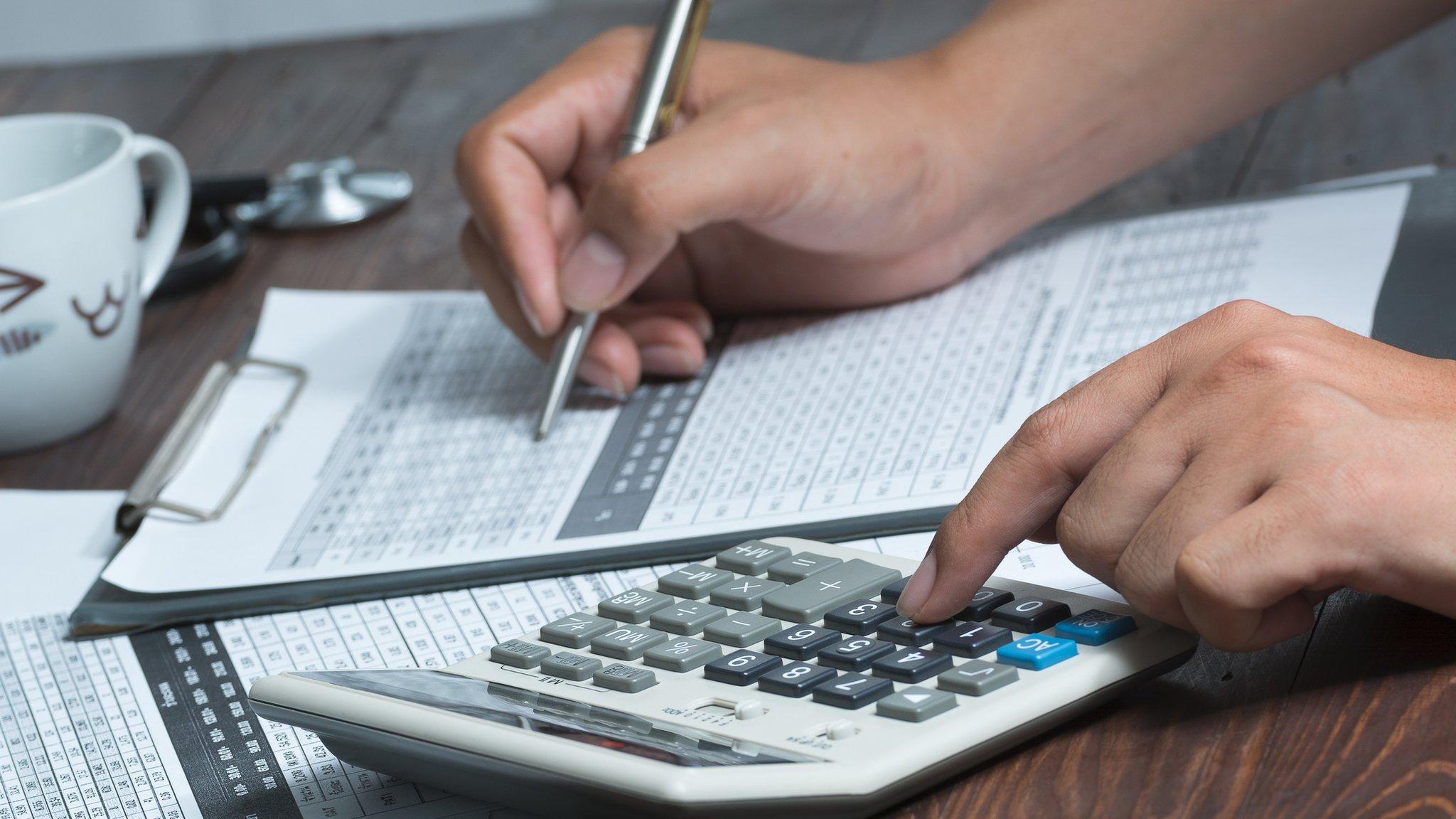 closeup of a young healthcare professional wearing a white coat calculates on an electronic calculator