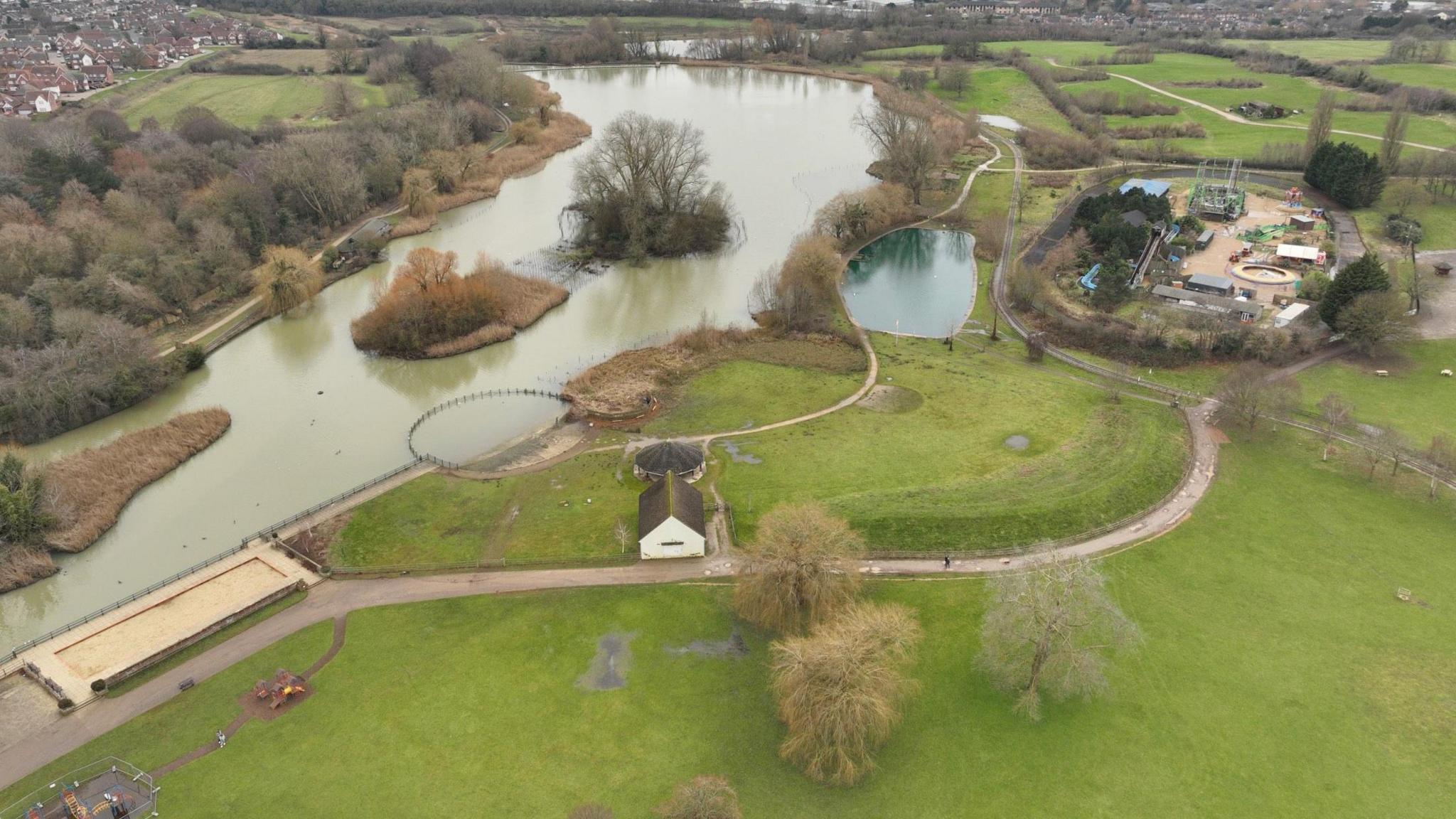 An aerial view of Wicksteed park with paths and a big lake.