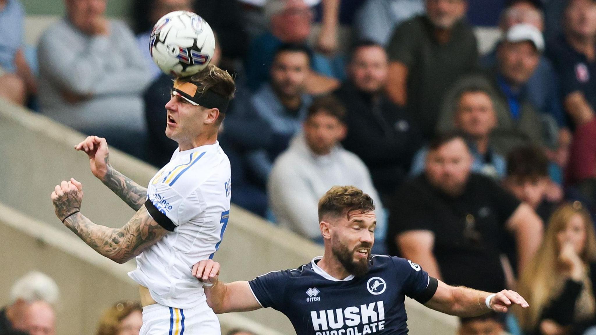 A bandaged Joe Rodon of Leeds heads the ball away under pressure from Millwall's Tom Bradshaw