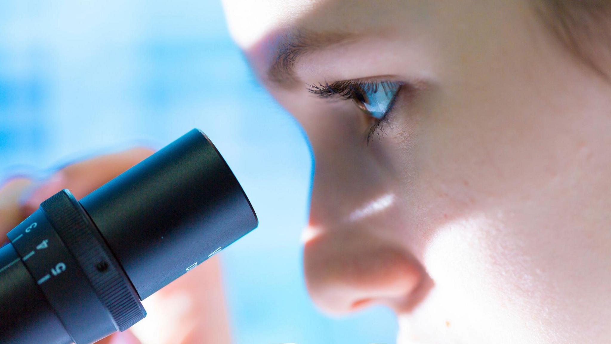 A close up of a person looking into a microscope