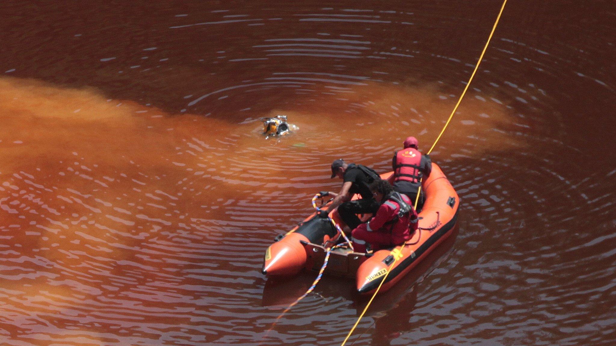 Forensic officers, rescuers and divers retrieve a suitcase, which police say contains a female body