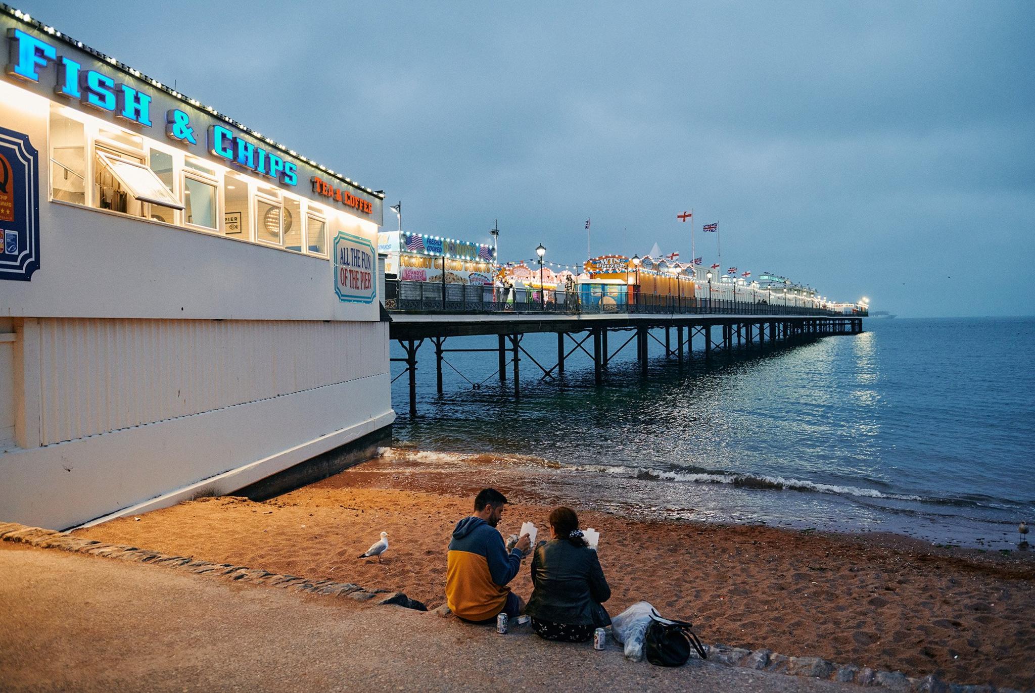 A couple enjoying fish and chips at dusk in Paignton