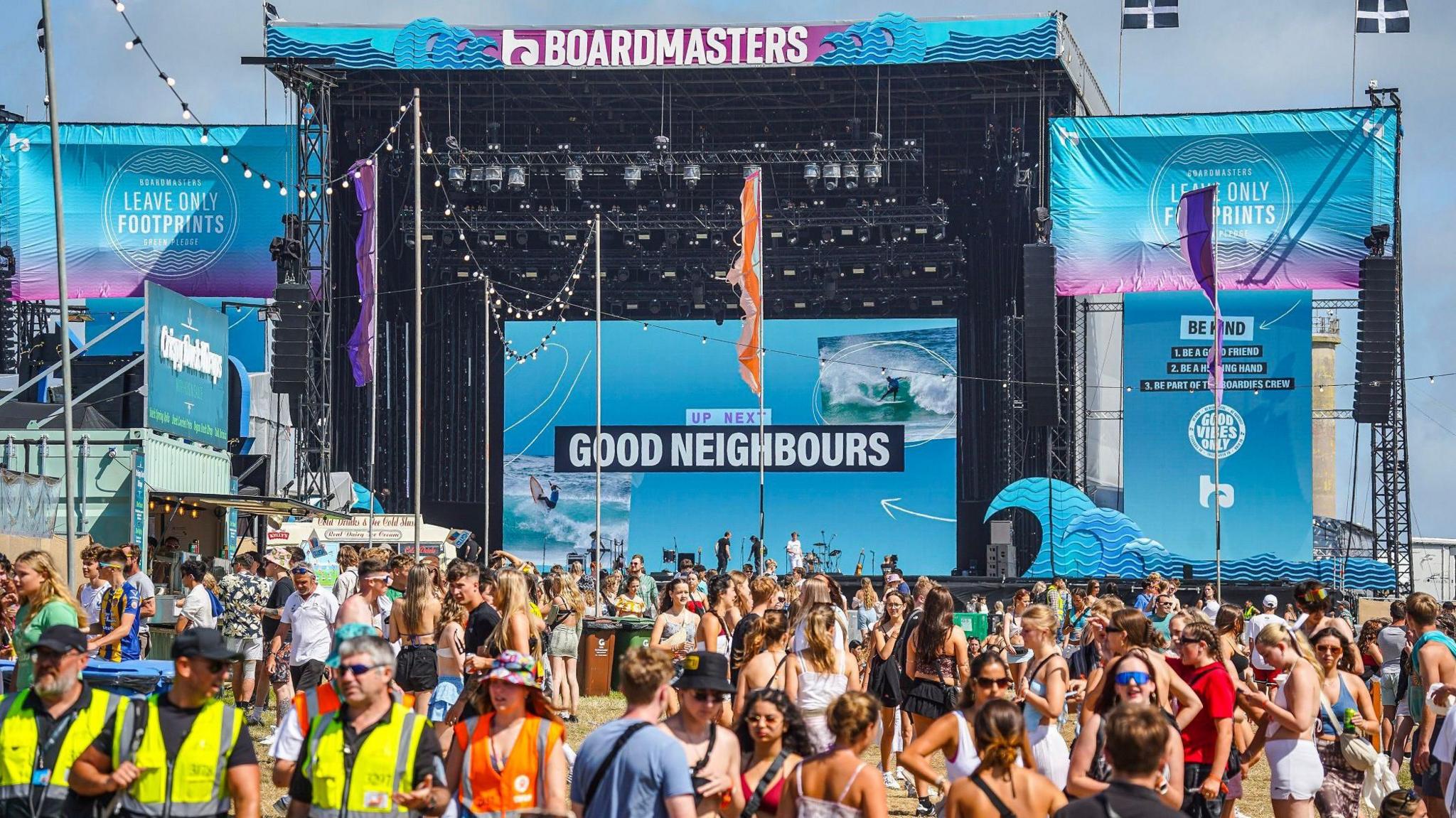 A crowd stand in the sunshine in front of the main stage at Boardmasters