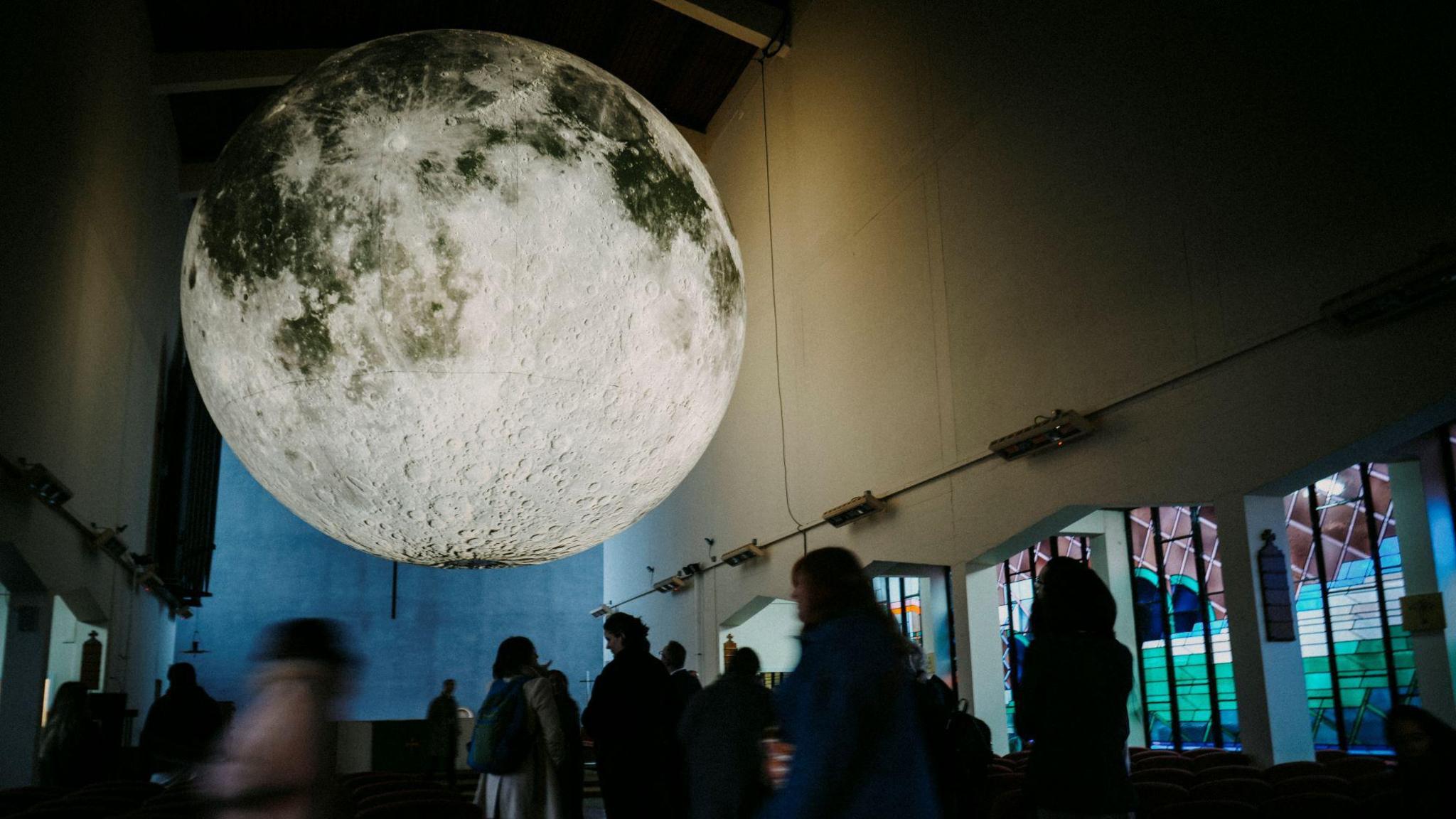 An image of a moon installation in a church and people looking at it.