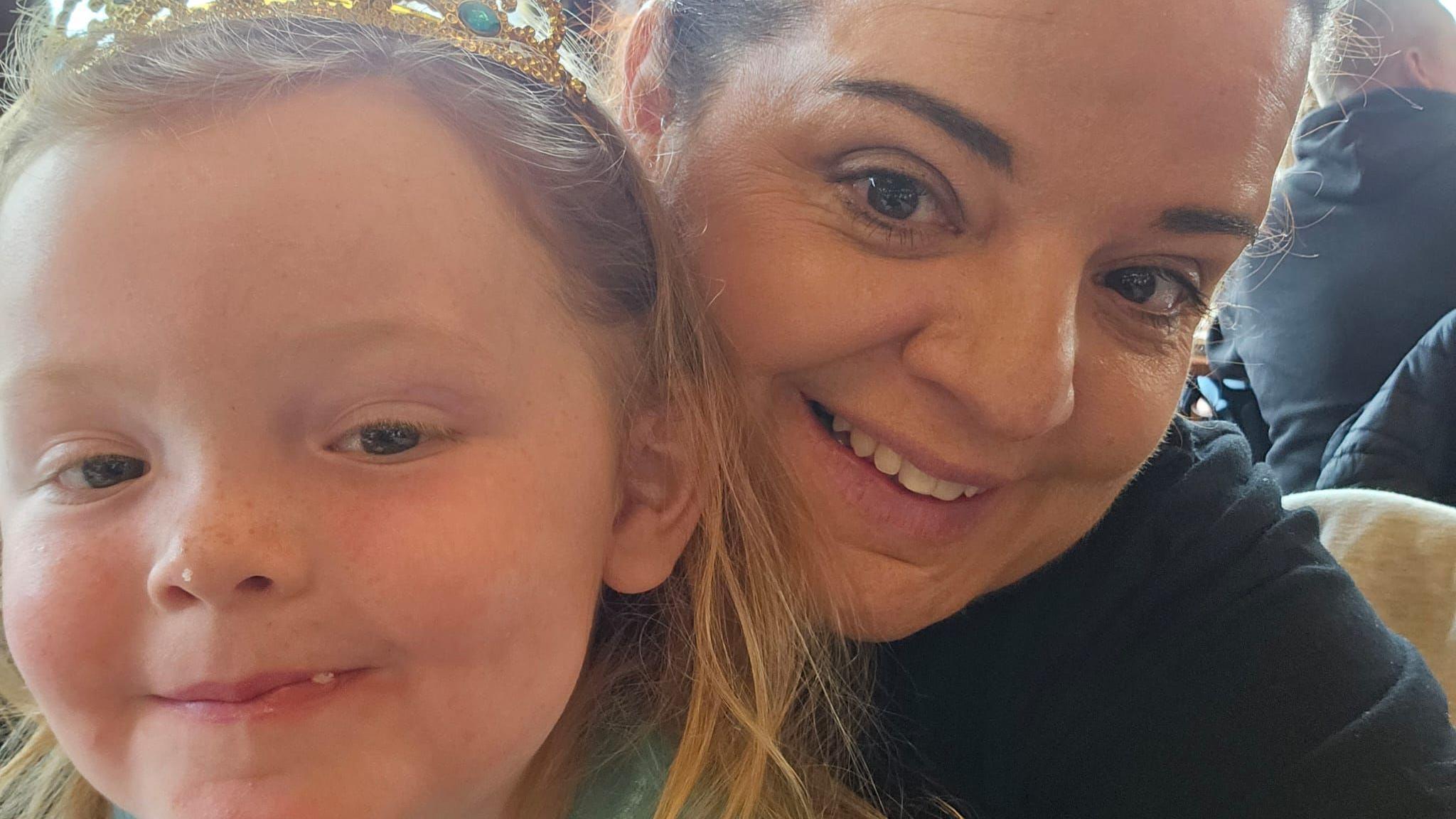 A selfie of Phoebe and Katie who are next to each other. Phoebe, on the left, has shoulder length ginger hair and is wearing a gold crown. Katie, on the right, has brown hair and is wearing a black T-shirt.