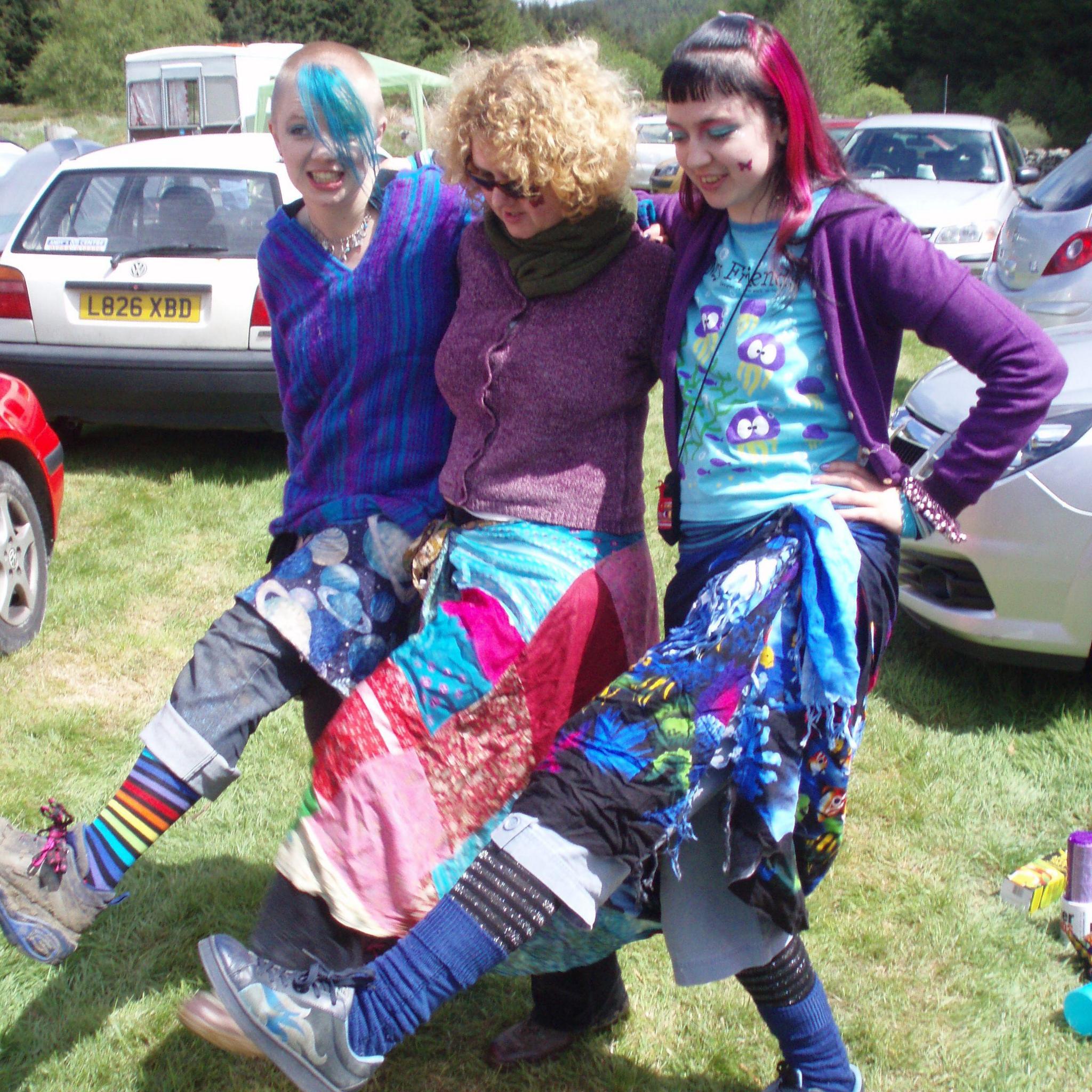 Tricia Hayes with her daughters, Stacey and Steff, kicking up their legs. They are wearing very colourful clothes.