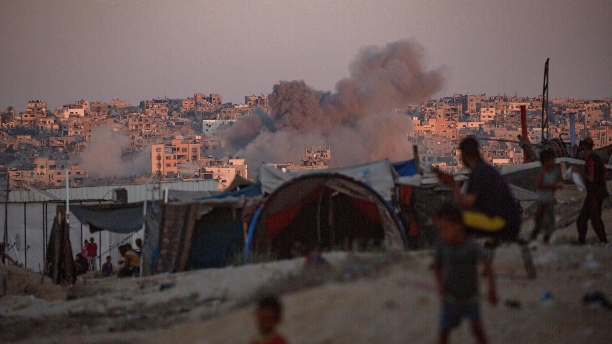 Smoke rises following an Israeli air strike, as displaced Palestinians sit next to tents in Khan Younis, southern Gaza (13 August 2024)