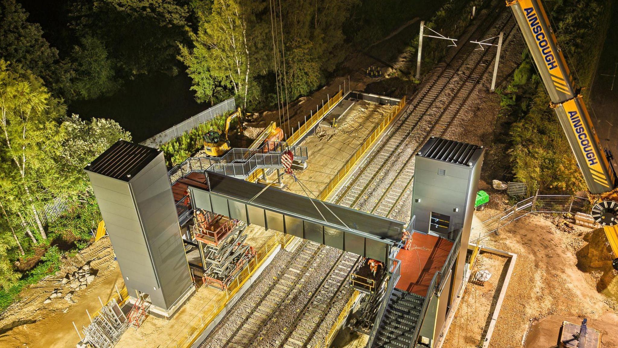 An aerial view of the construction site of the new Tram Train Magna stop. Central to the image are two very new lift shafts with an adjoining bridge surrounded by construction equipment. Below are tram tracks.