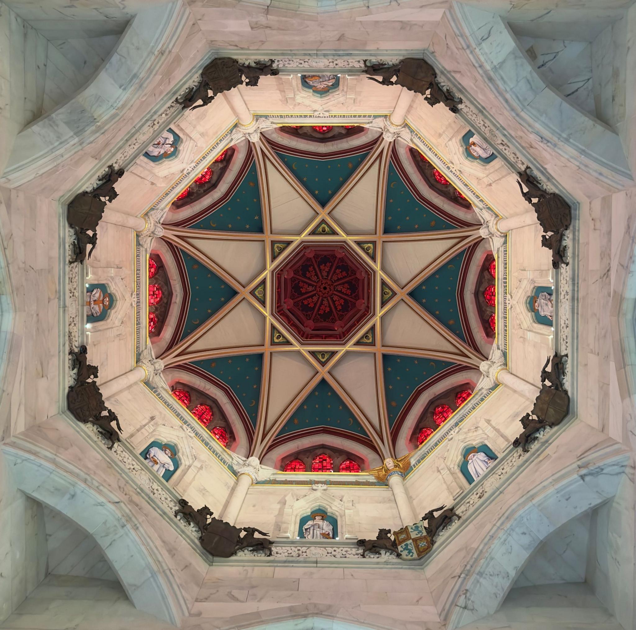 Ceiling of a church, taken from the floor below, showing an octagon style shape with a star shape formed in stained glass, coloured in blue, red, white, and gold