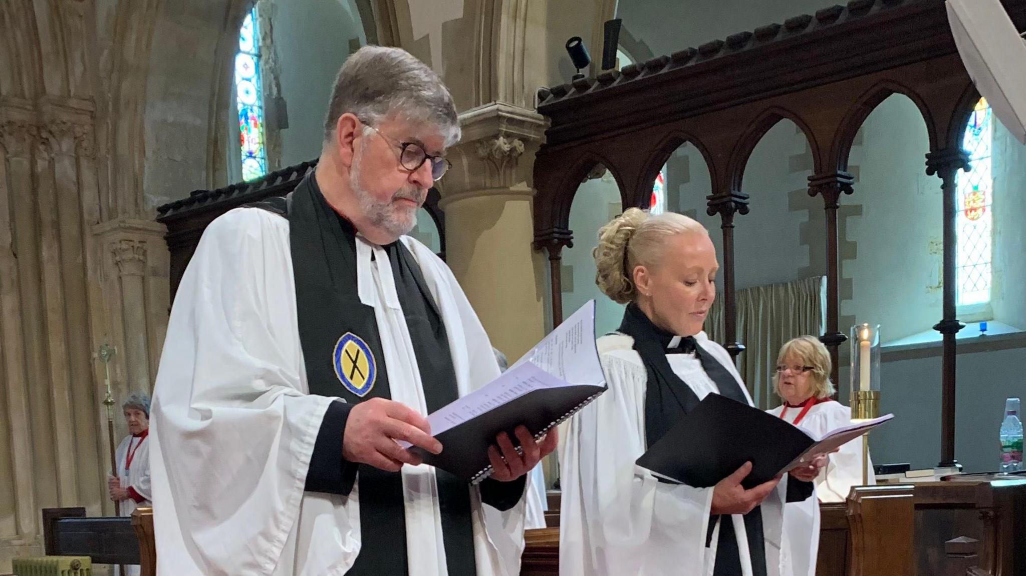 Very Reverend Tim Barker on the left reading from a black book. On the right is Reverend Samantha Martell who is also reading from a black book.