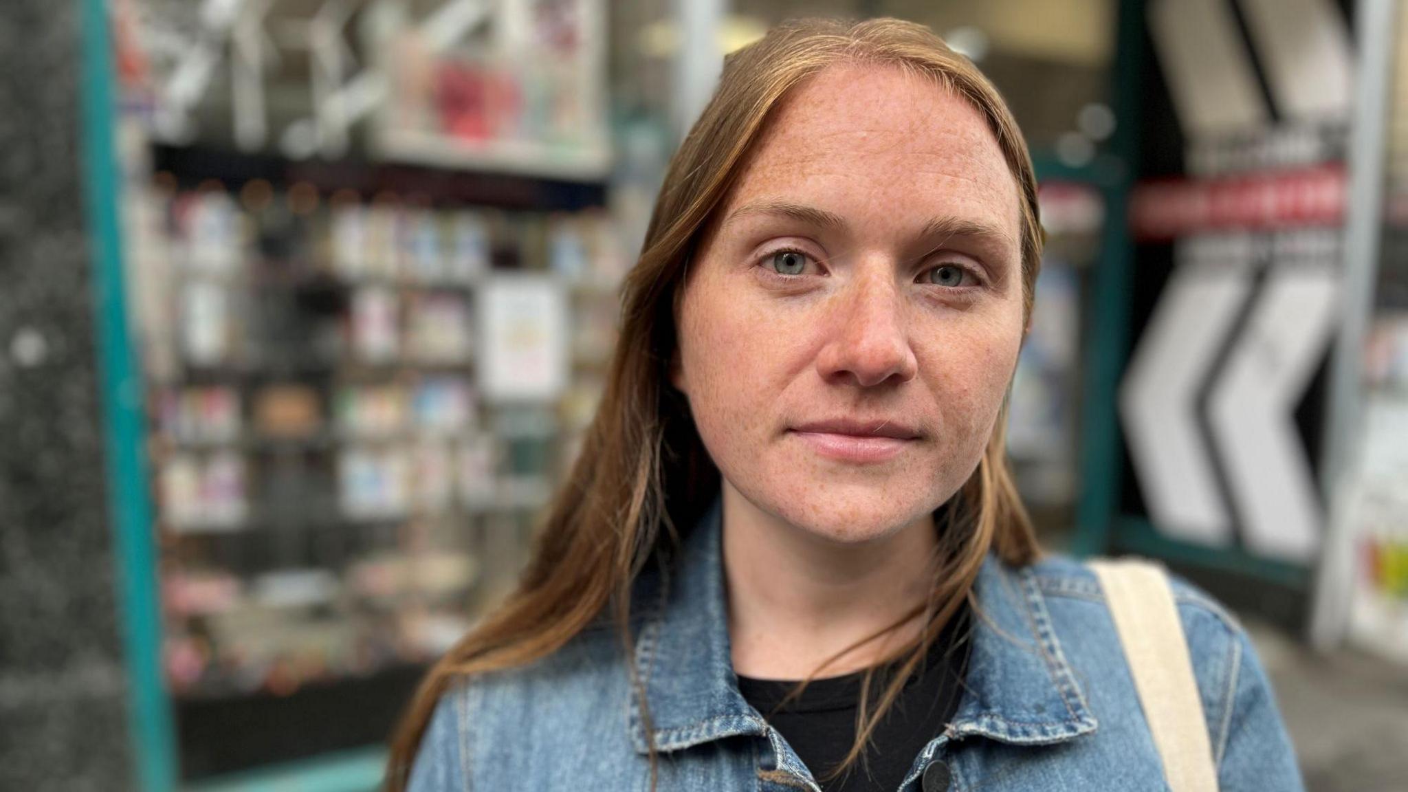 Laura Young, in a denim jacket over a black top, standing outside a shop with vapes displayed in the window.