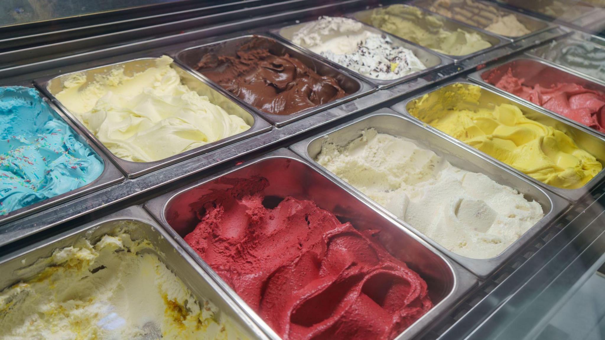 A vibrant array of creamy Italian gelato. We can see chocolate, berry, pistachio, vanilla, lemon. They are arranged in a chilled showcase at an artisan ice-cream shop.