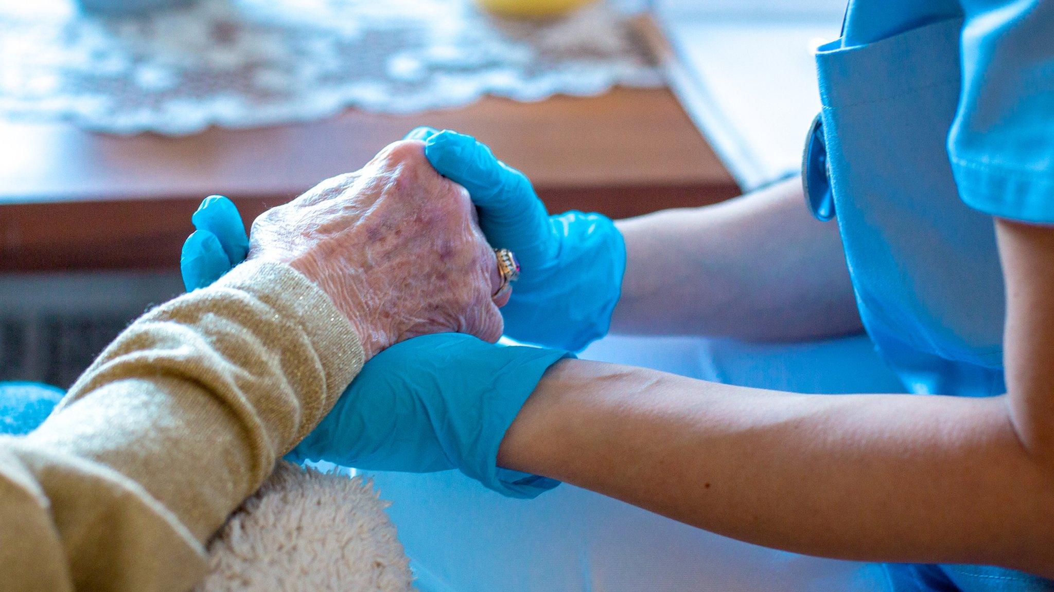 A carer holding the hand of an elderly person