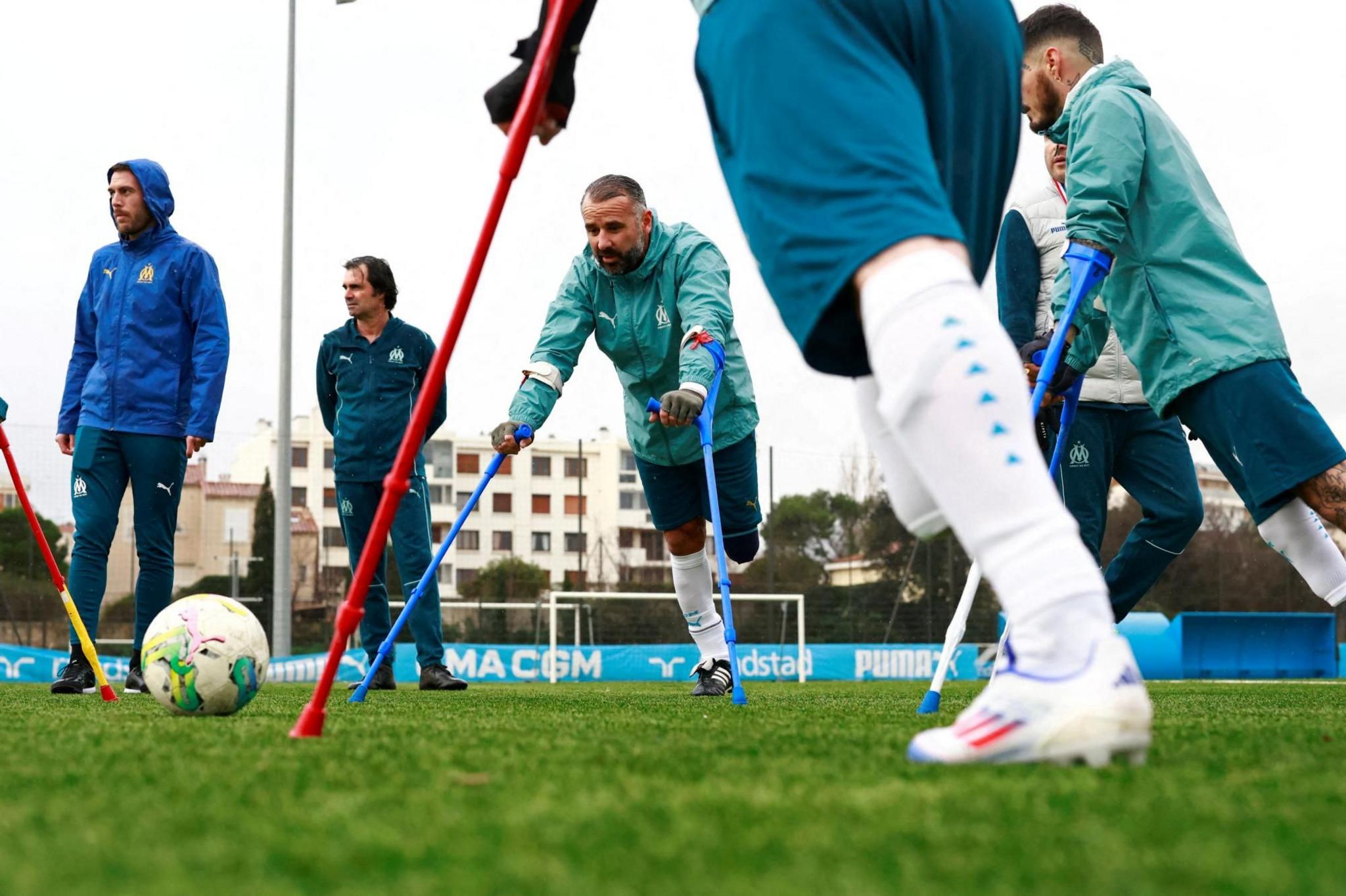 Amputee footballers attend a training session. Six men are pictured. Three are amputees on crutches. The football is to the left of the picture and two of the men on crutches are looking at it.