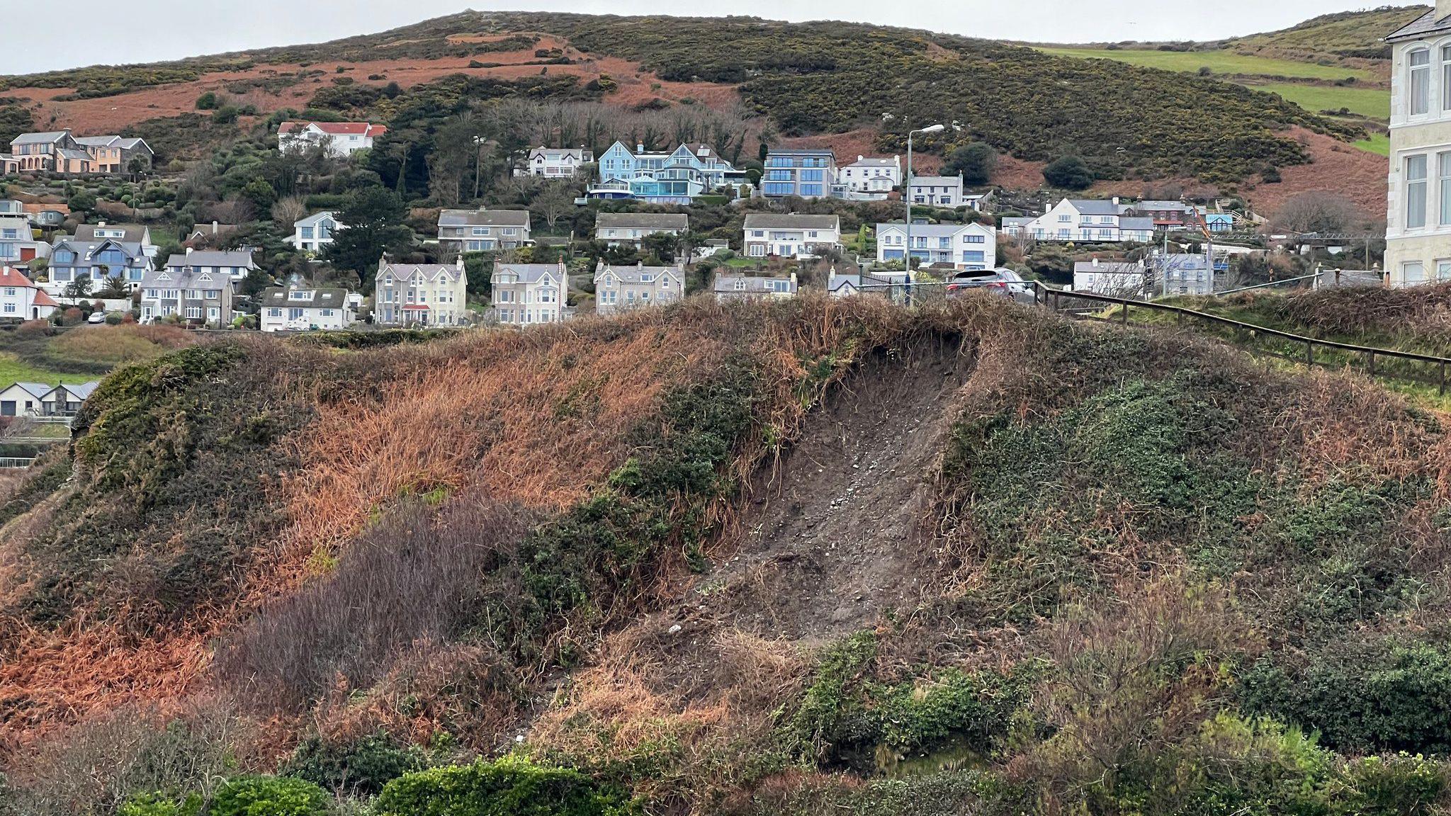 Grassy hilly terrain with large muddy patches where land has slipped. 