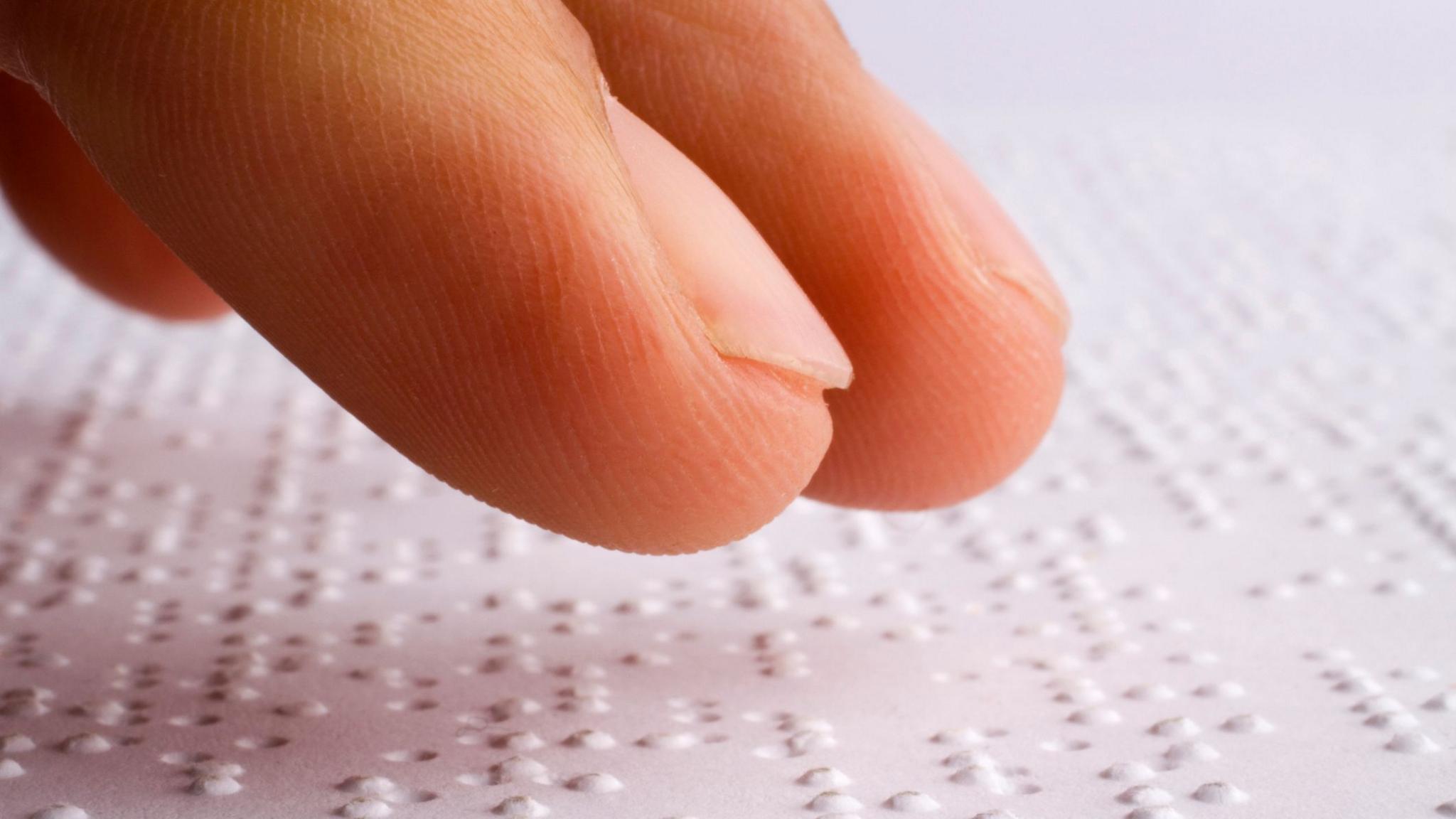 Finger tips above a page of Braille