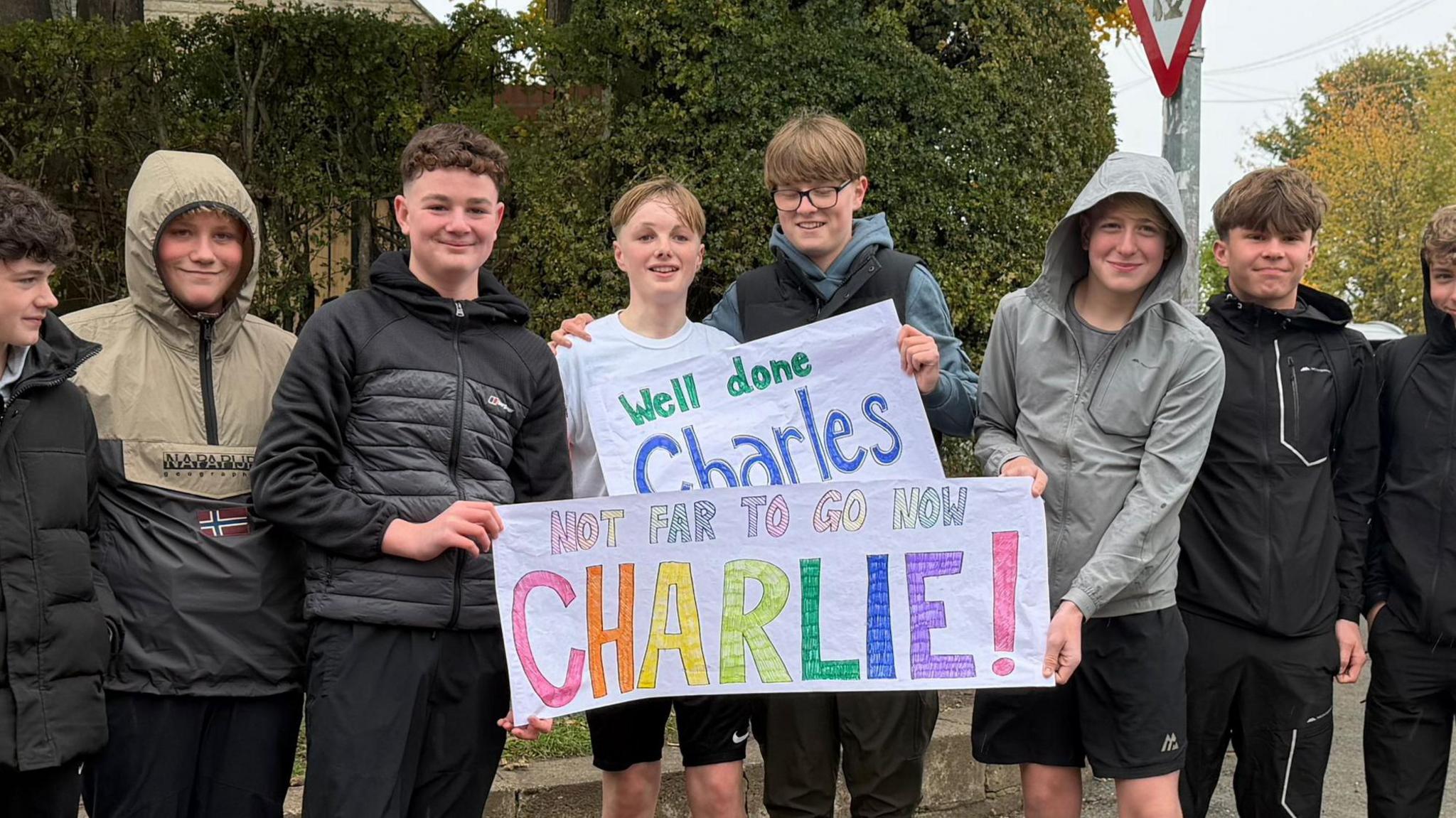 Charlie Graver with his friends who are holding banners reading 'Well done Charles' and 'Not far to go now Charlie'.