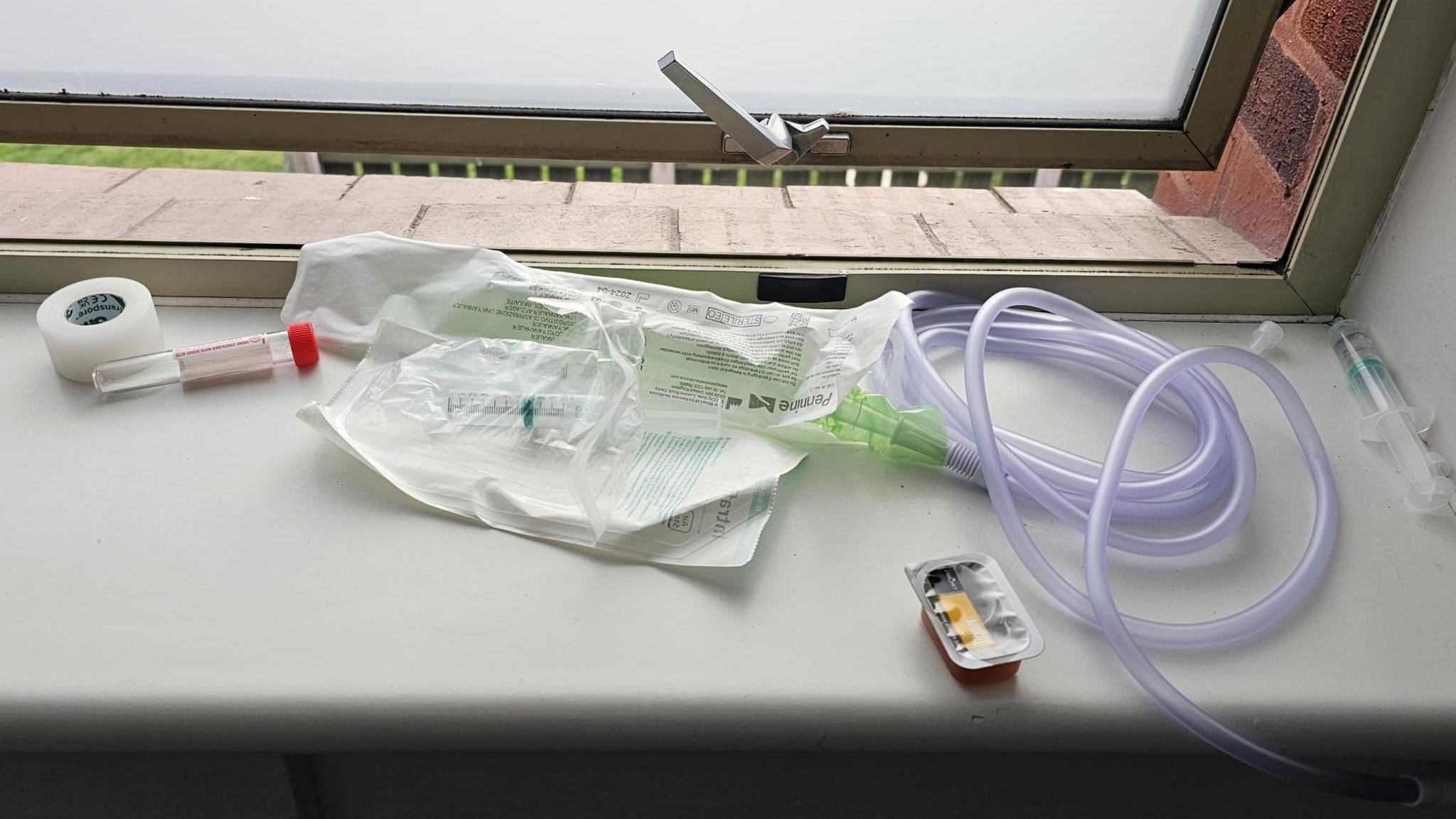 Tubes and what appears to be a syringe on a hospital window. You can see at least one of the syringes has liquid in.