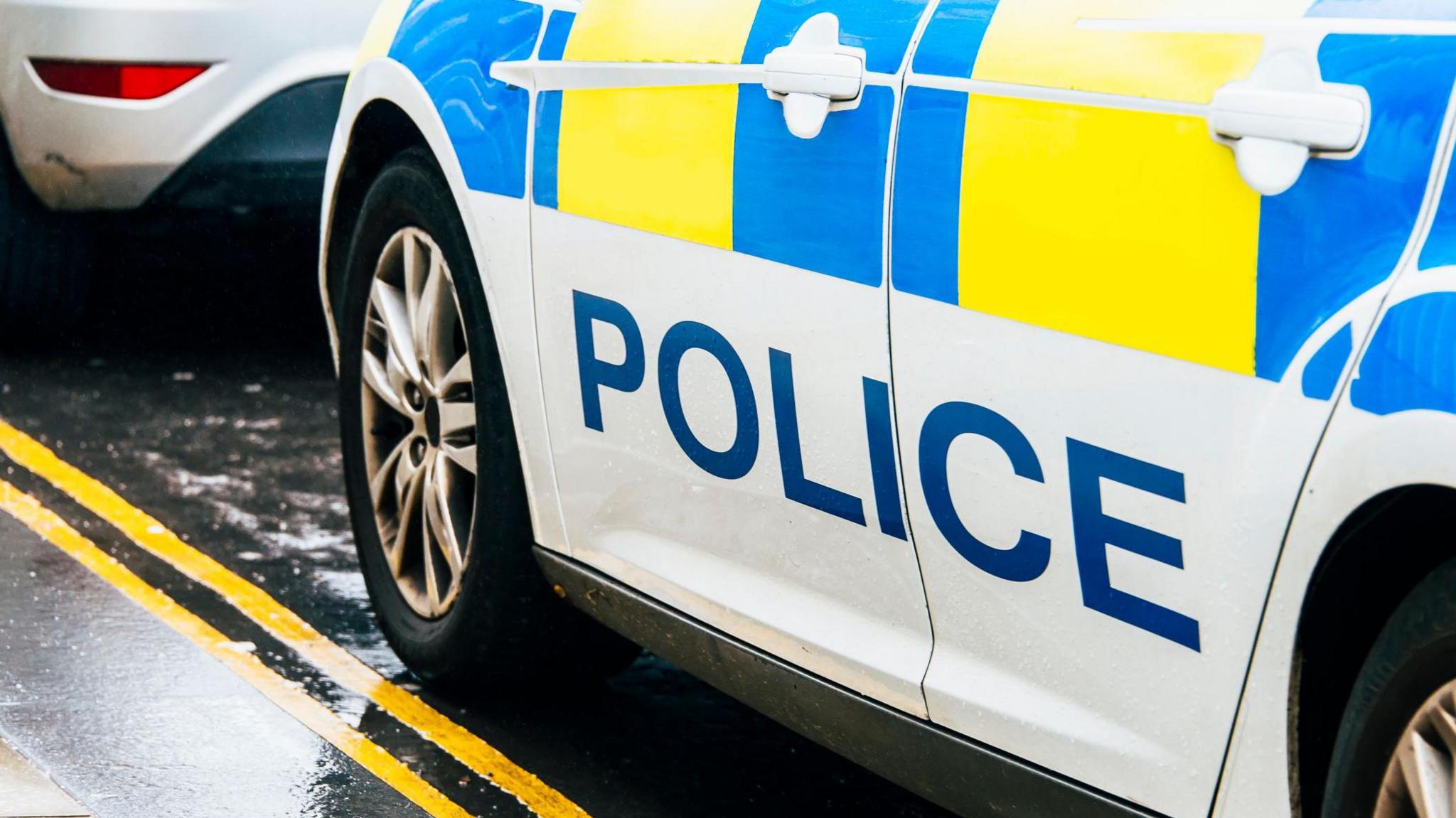 A stock image of a Police Scotland car - the image is cropped from the vehicle's door handles to a set of double yellow lines on the road below.